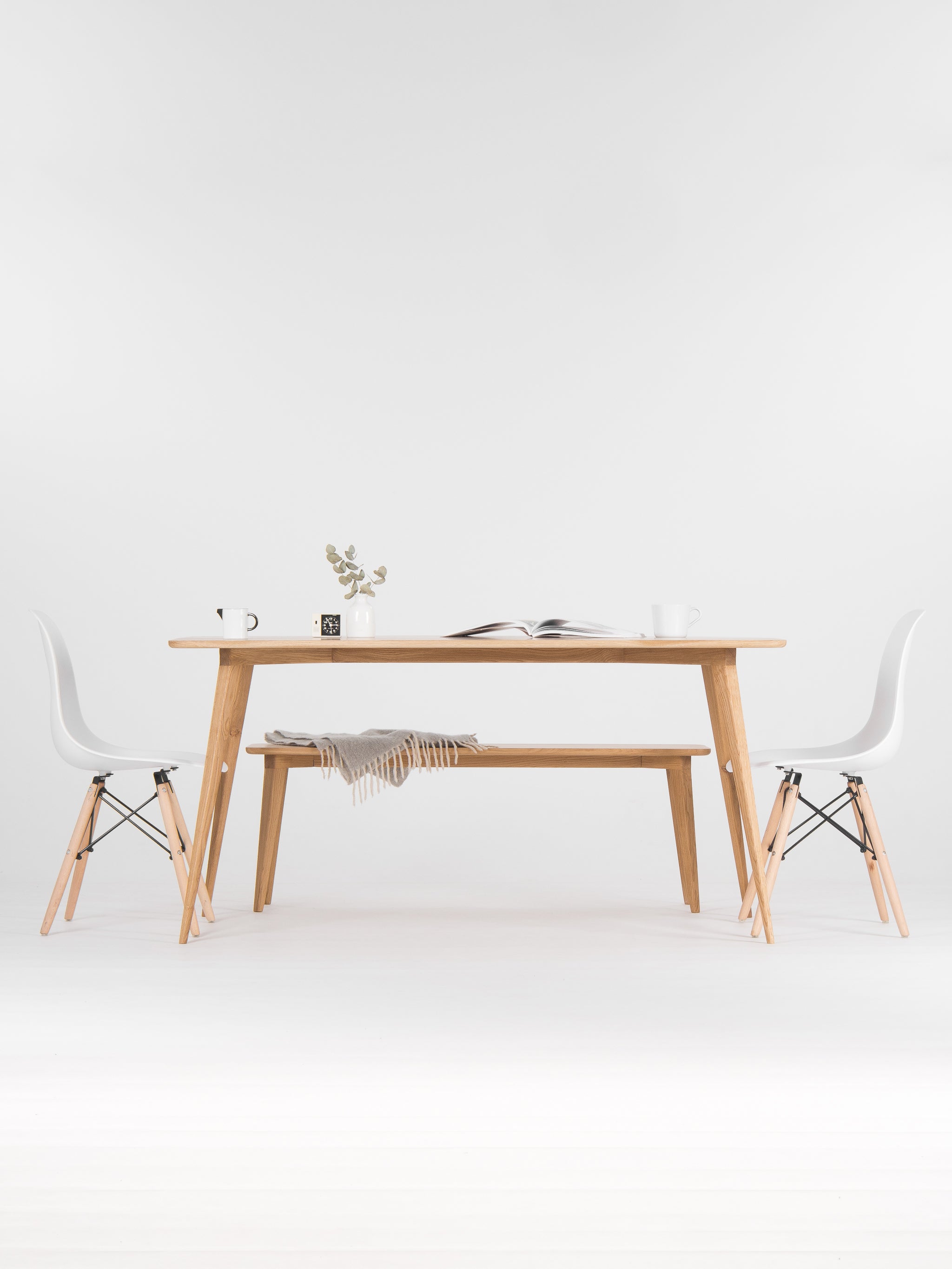 Minimalist dining area with a wooden table, chairs, a vase, and an open book.
