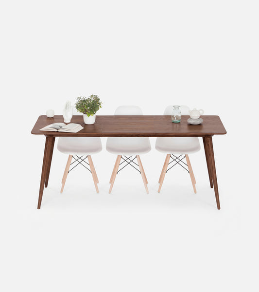 A wooden table with white chairs, a potted plant, and a book on top.