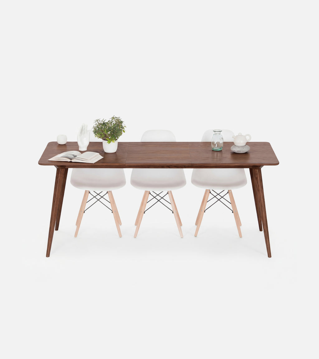 A wooden table with white chairs, a potted plant, and a book on top.