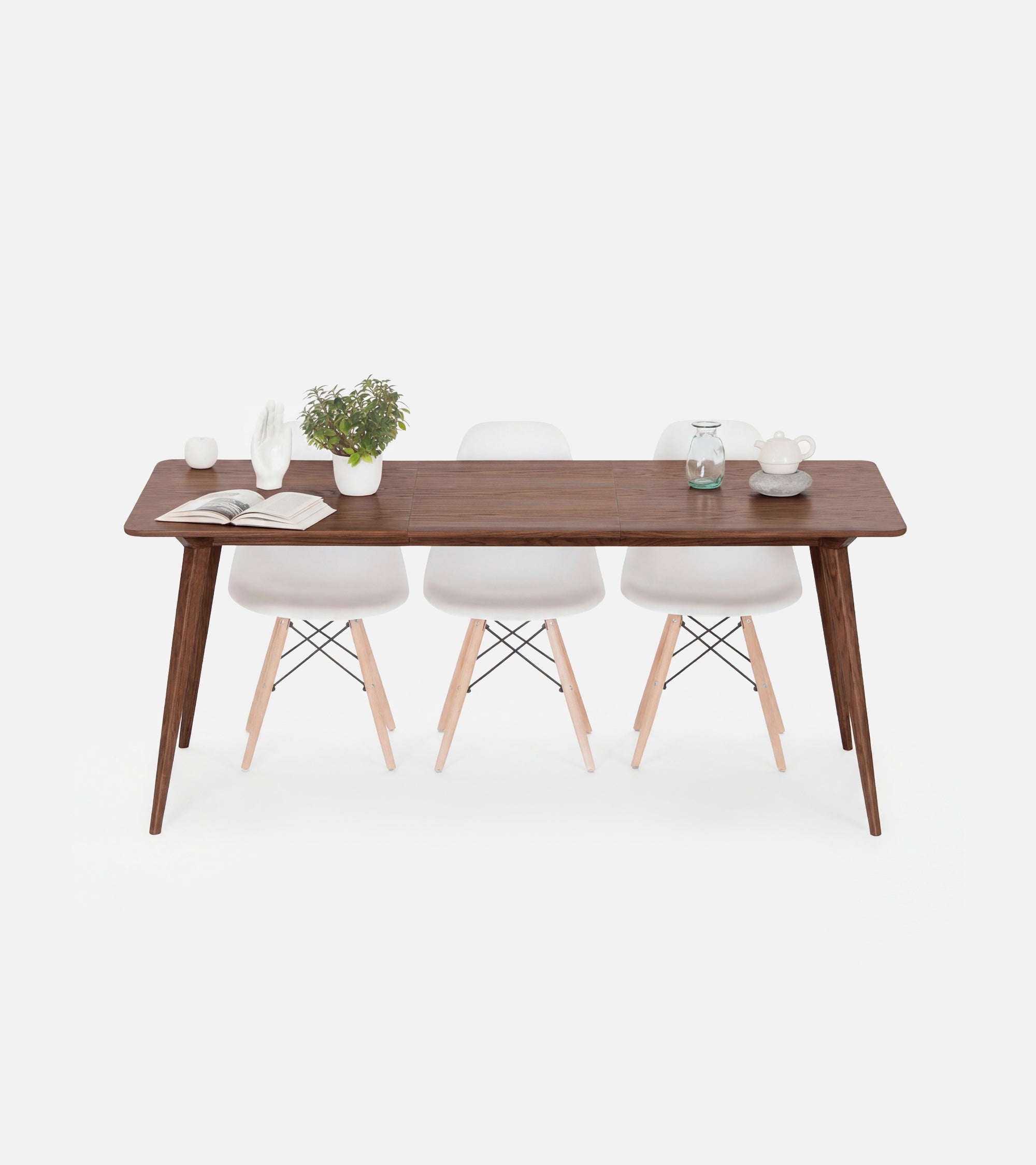 A wooden table with white chairs, a potted plant, and a book on top.