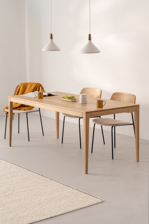 Minimalist dining area with a wooden table, two chairs, pendant lights, a mustard throw, and a plate of grapes.