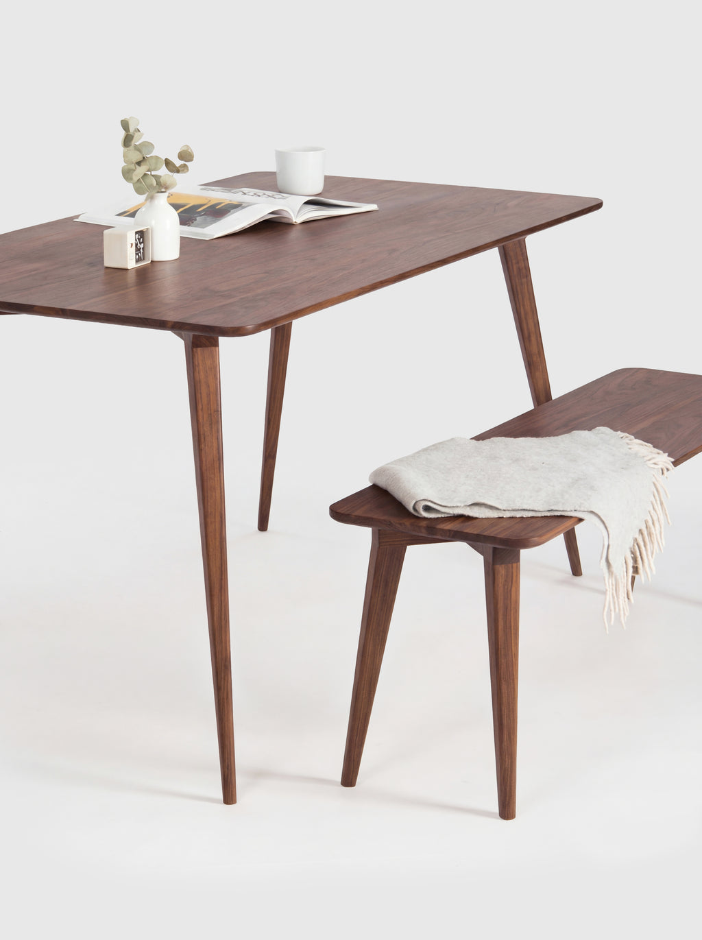 Stylish wooden table with a bench, magazine, cup, and plant on top.