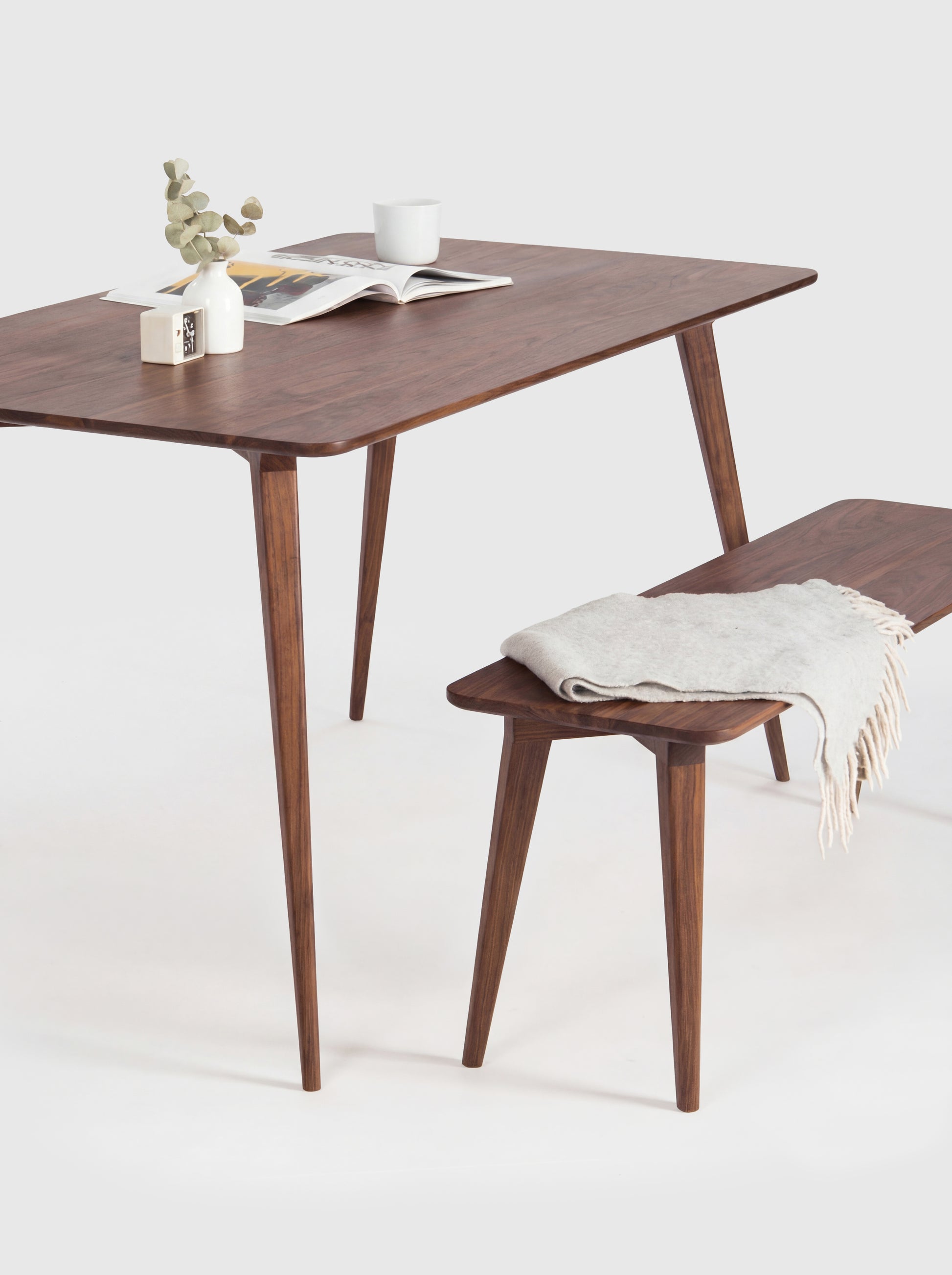 Stylish wooden table with a bench, magazine, cup, and plant on top.