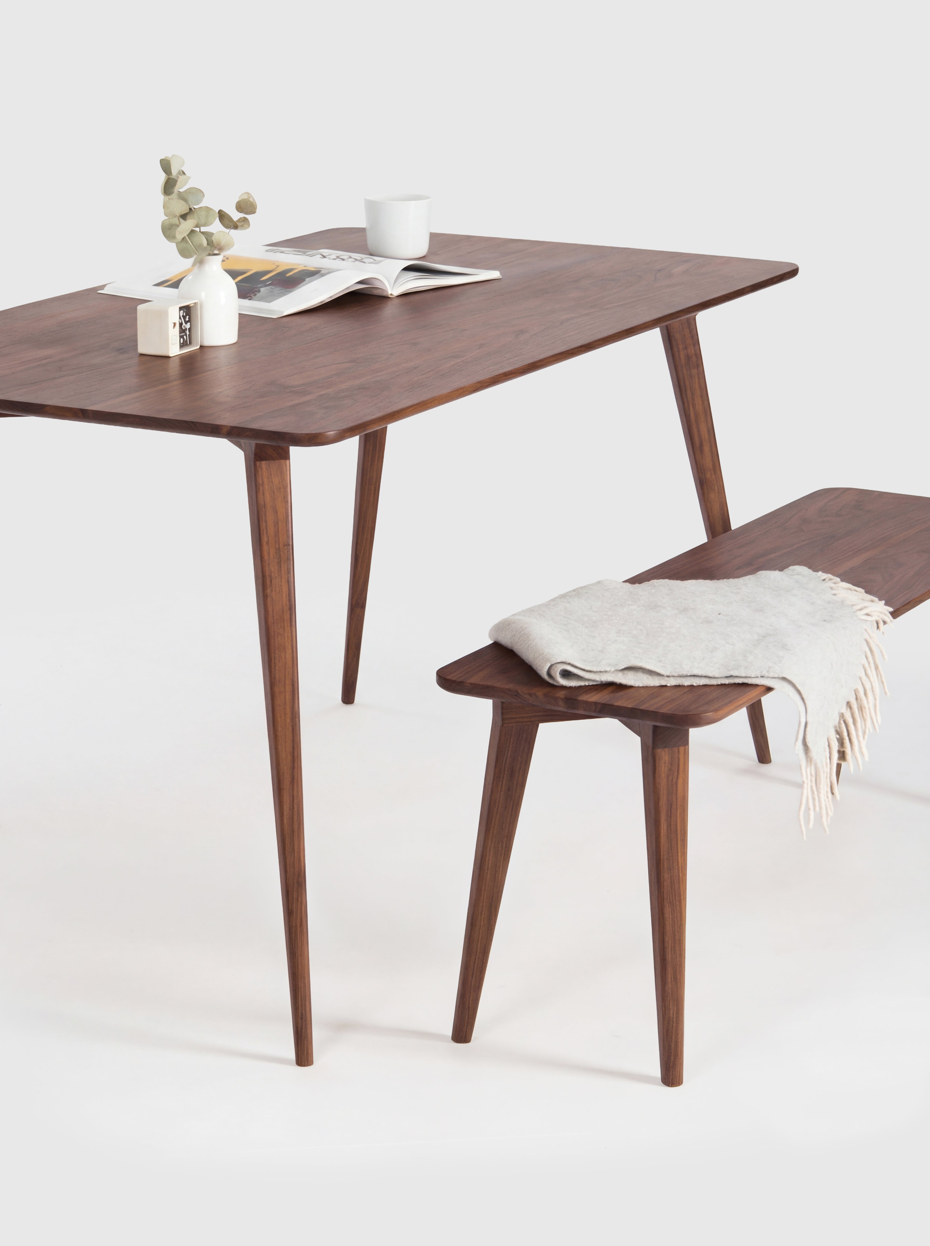 Stylish wooden table with a bench, magazine, cup, and plant on top.