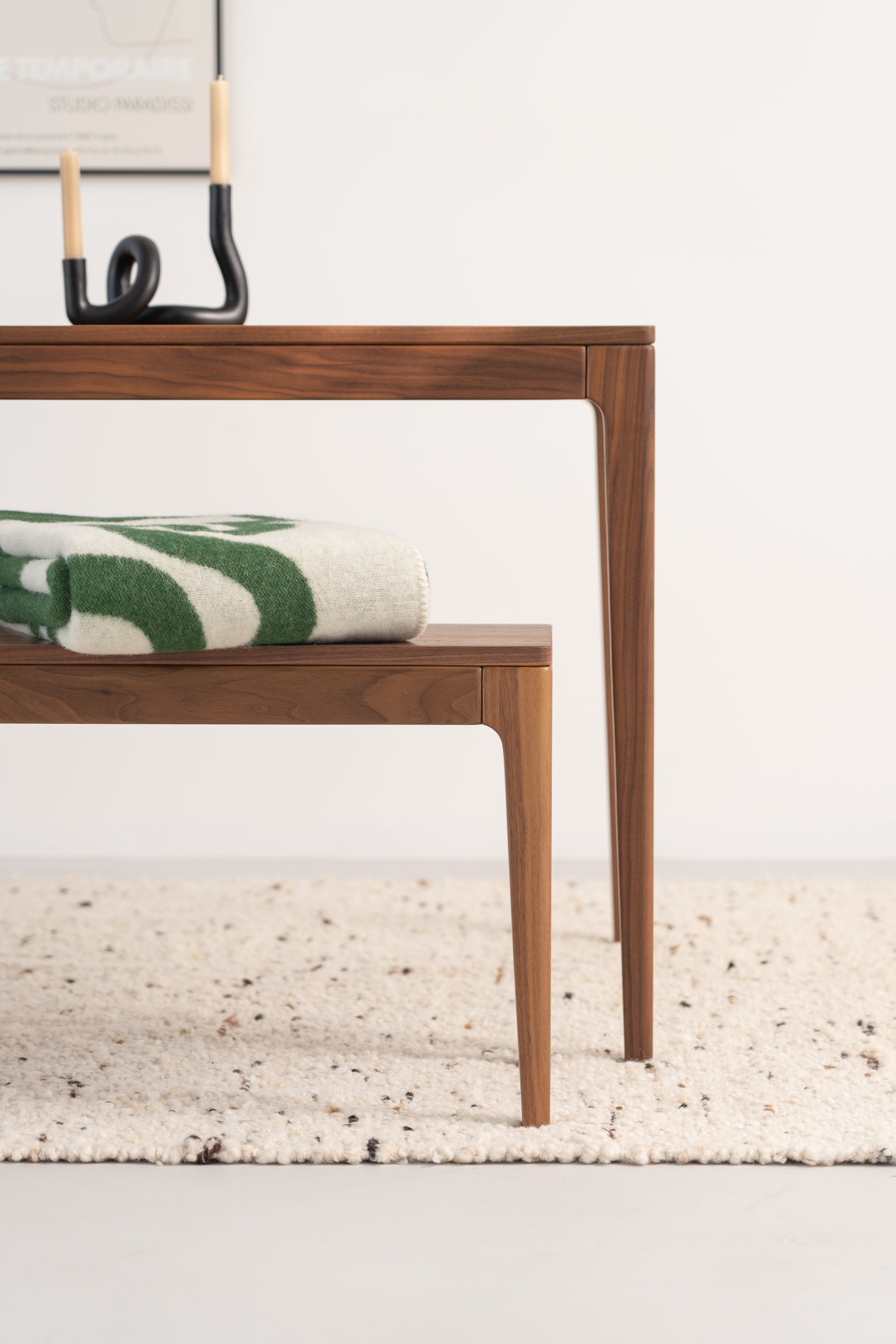 Wooden table and bench with a folded green and white blanket on a textured rug.