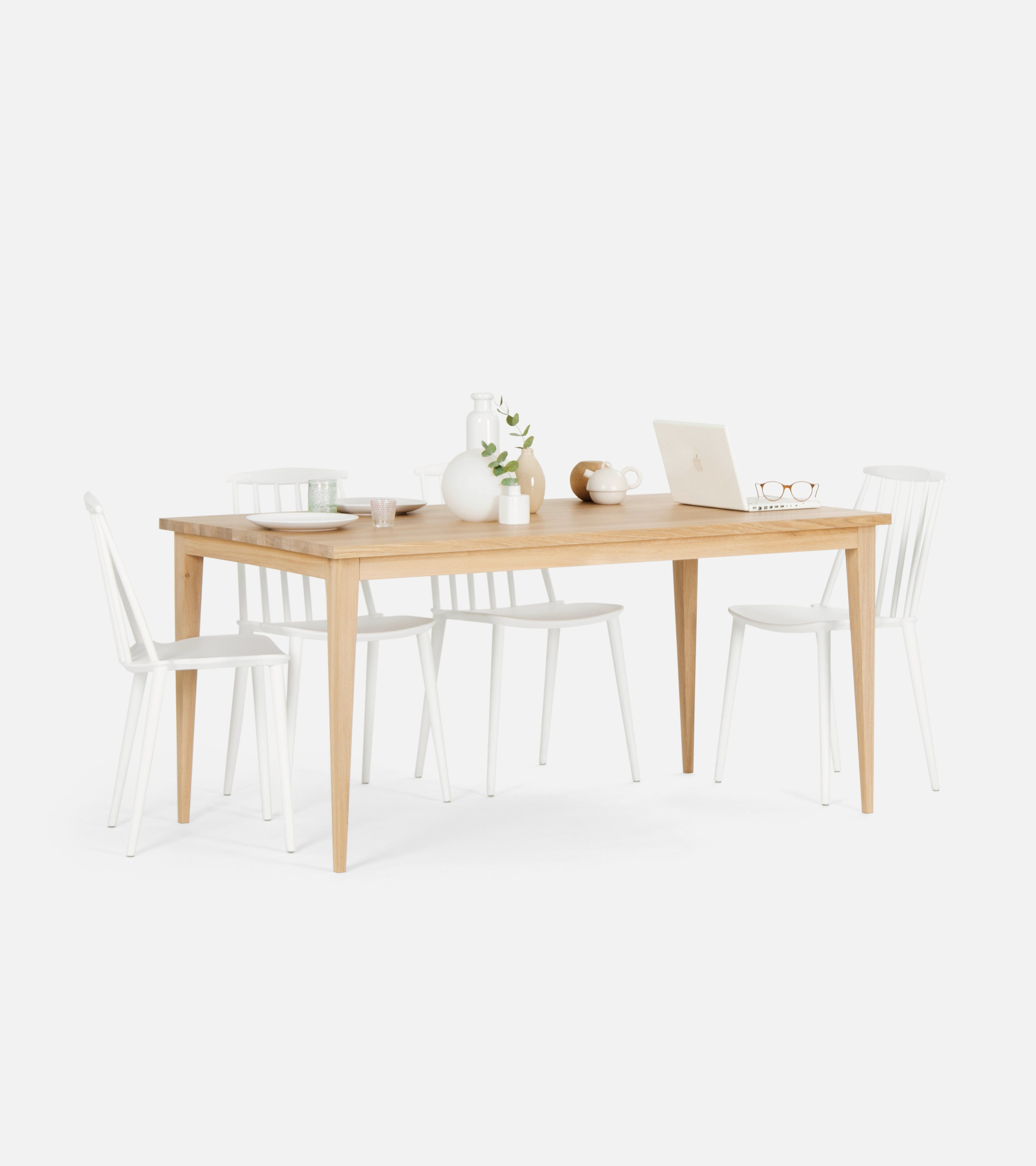 A wooden dining table with white chairs, set with a laptop, plates, glasses, and various decorative items.