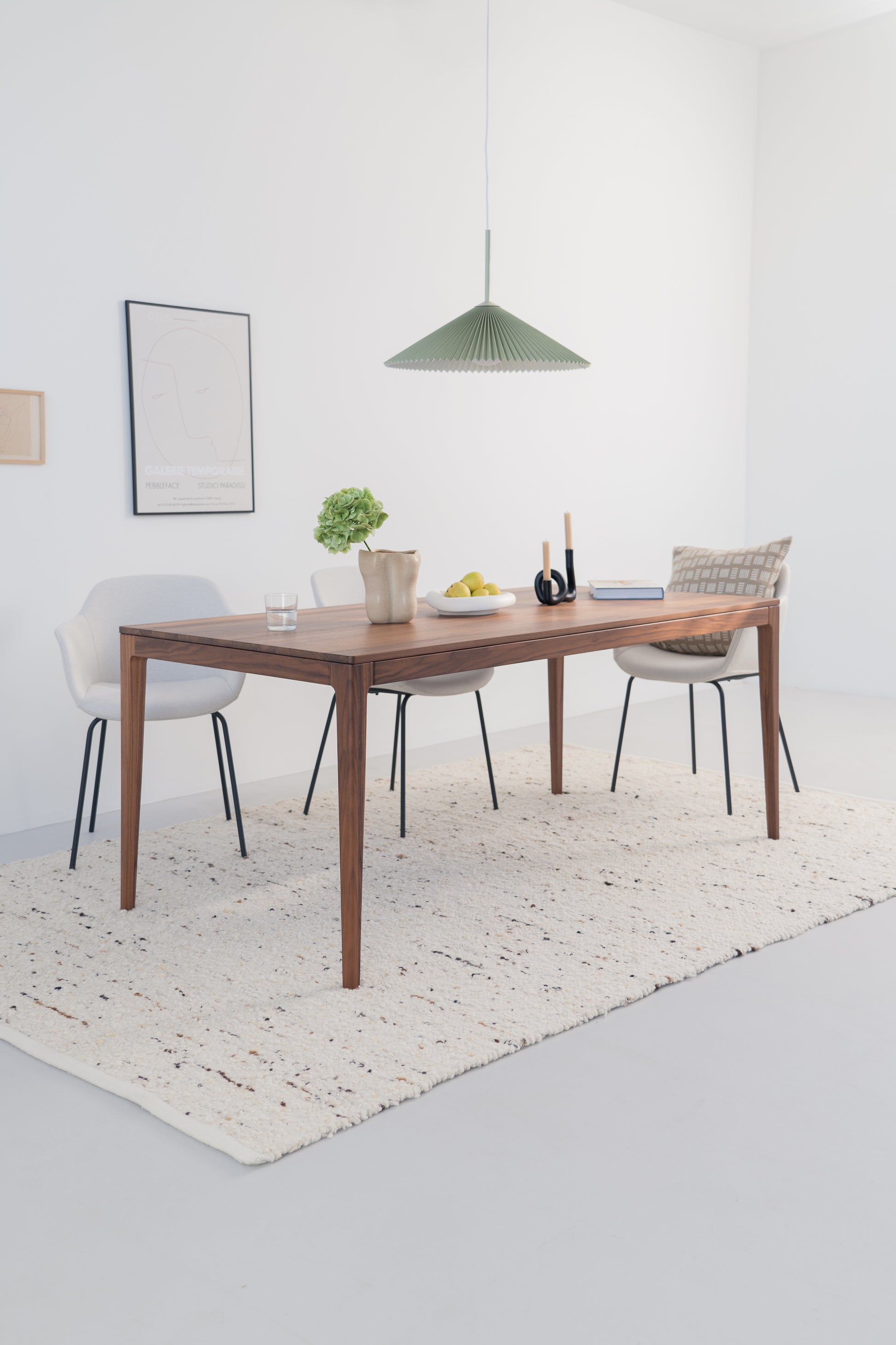 Minimalist dining area with wooden table, chairs, green pendant light, and a white rug.
