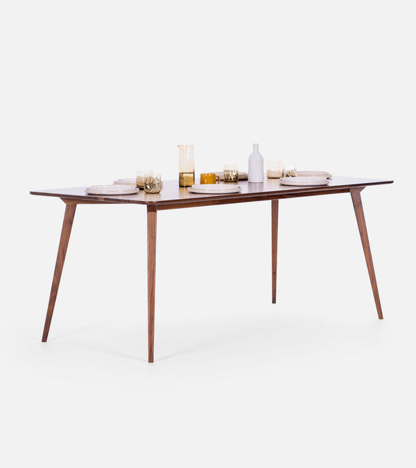 A wooden dining table set with plates, glasses, a pitcher, and a bottle on a white background.