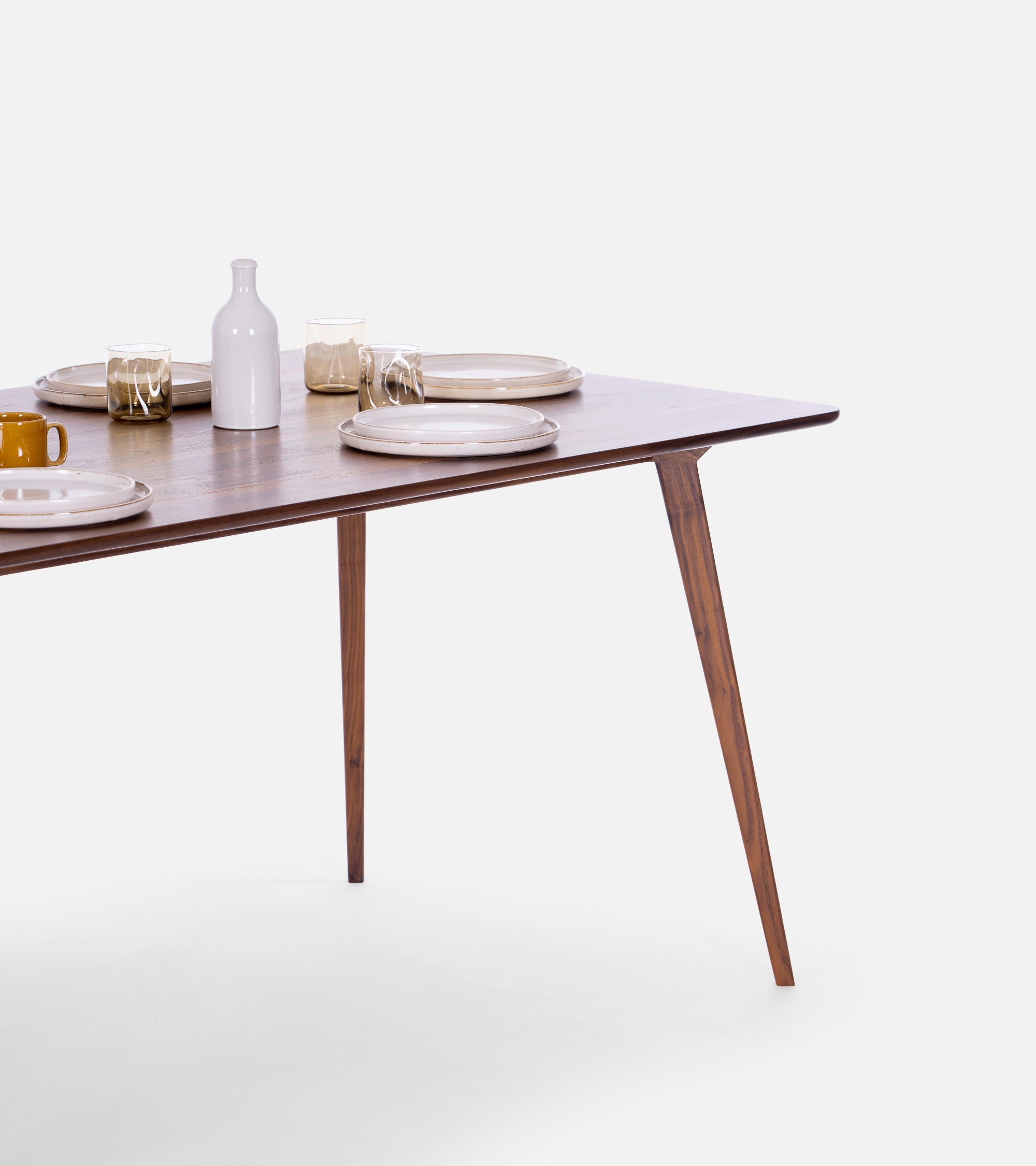 A wooden table set with plates, glasses, and a bottle.