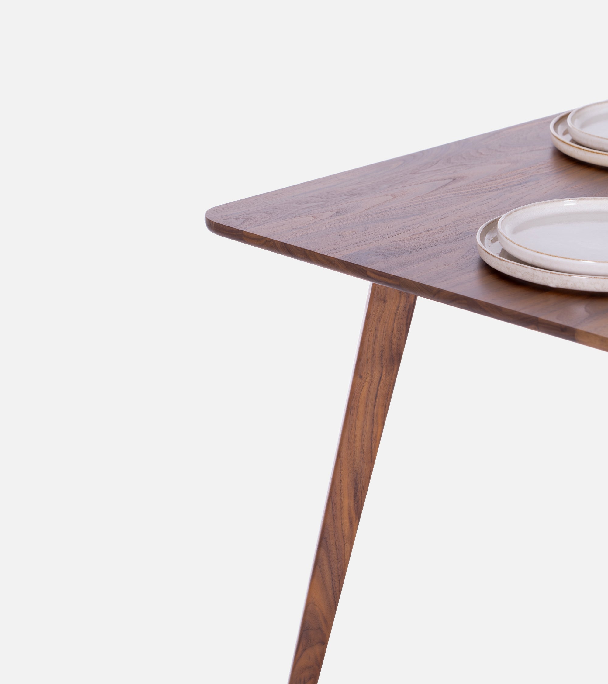 Corner of a wooden table with three stacked plates on it, against a plain white background.