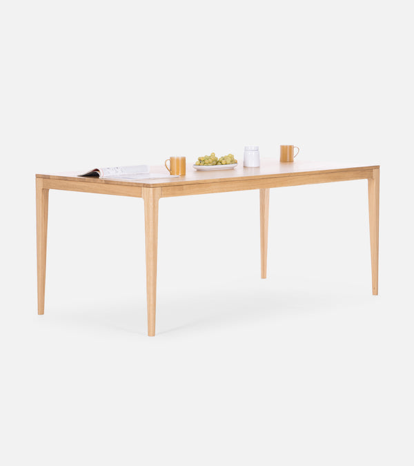 A wooden table with cups, a plate of grapes, a mug, and an open book on it against a white background.