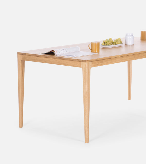 Wooden table set with an open book, mug, plate of green grapes, and a white container against a plain background.