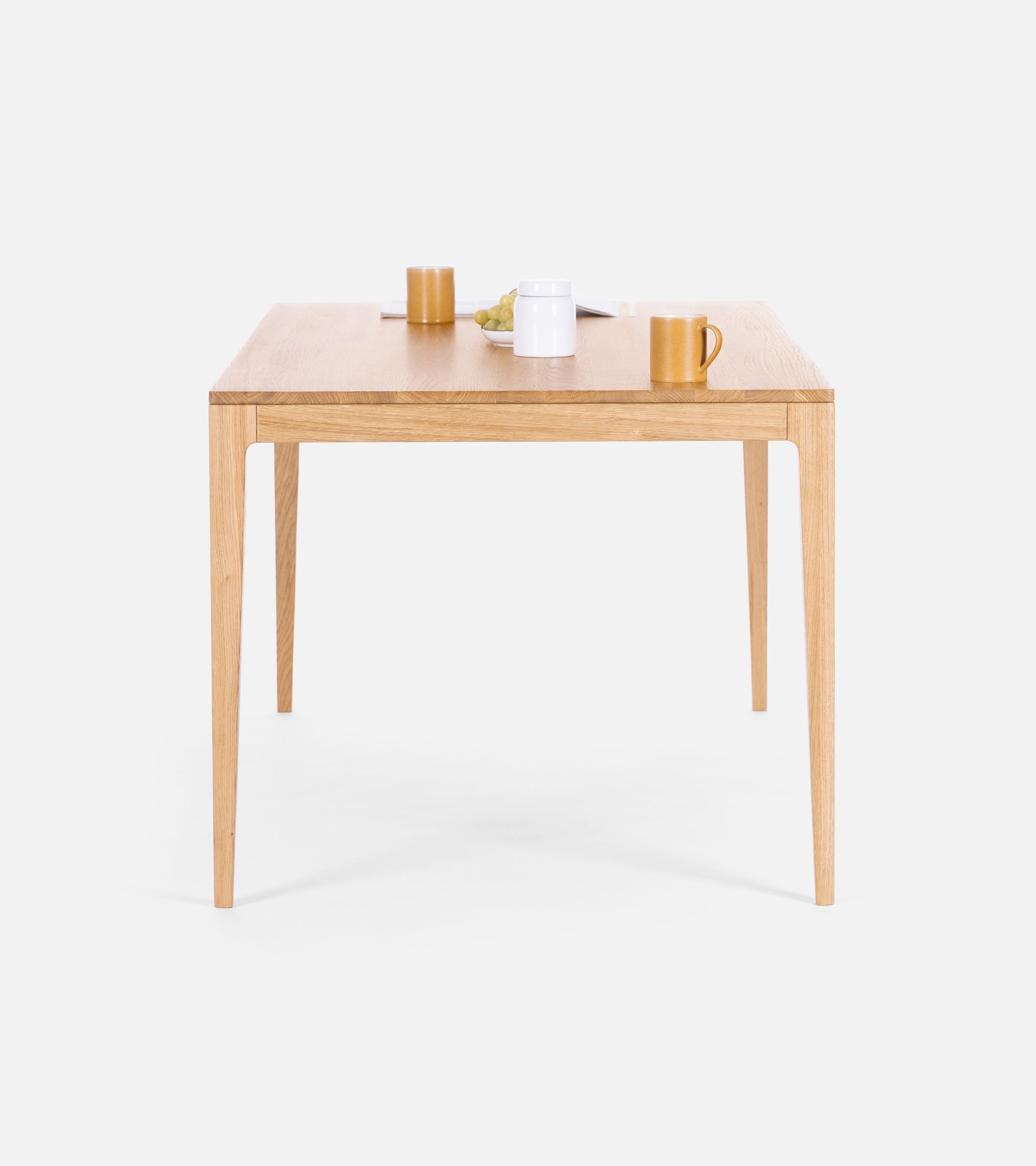 A wooden table with a simple design, featuring a white mug, yellow cups, and a plate of grapes on top.