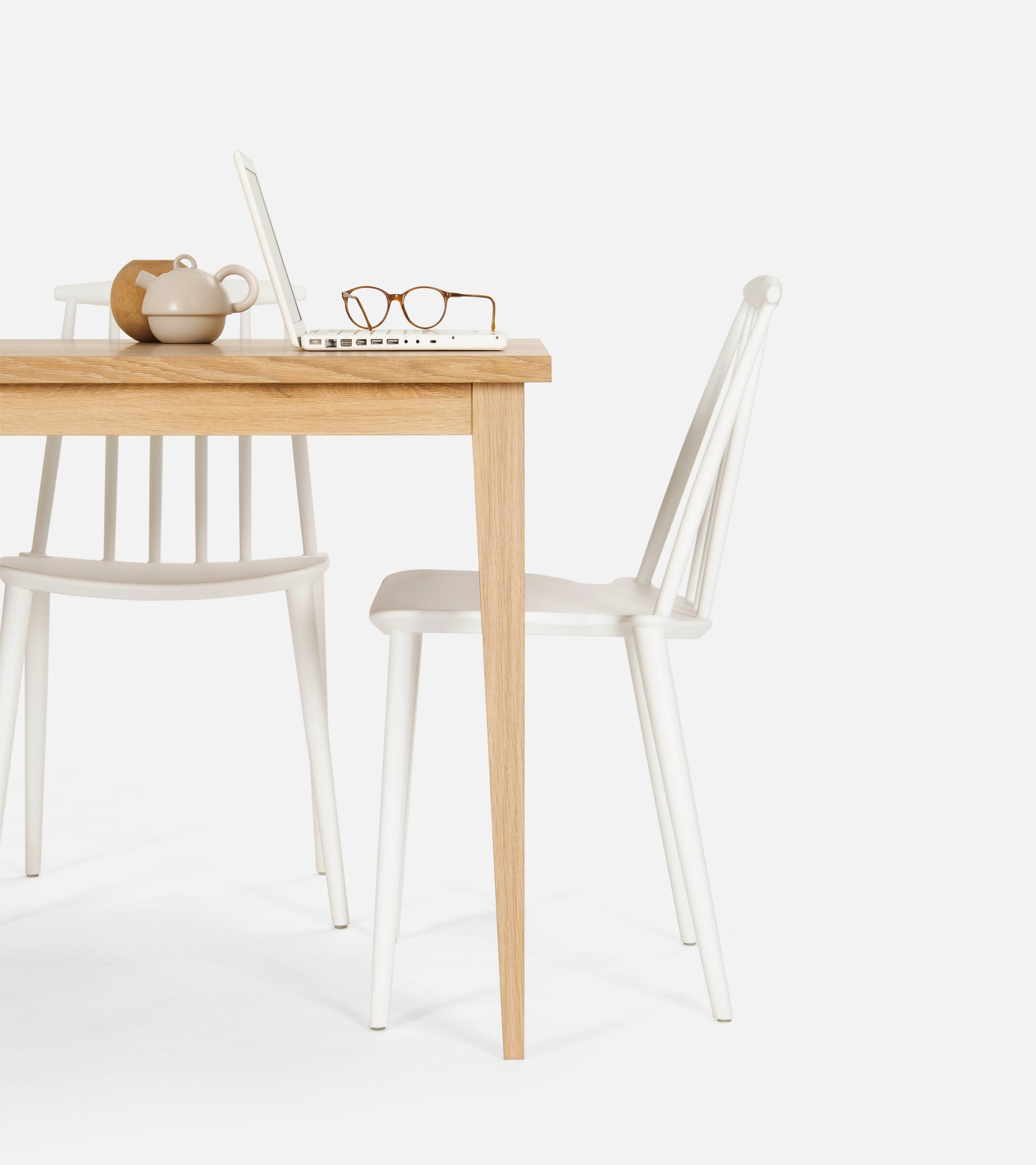 A wooden table with a laptop, glasses, and a teapot; two white chairs are placed nearby.