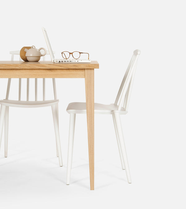 A wooden table with a laptop, glasses, and a teapot; two white chairs are placed nearby.