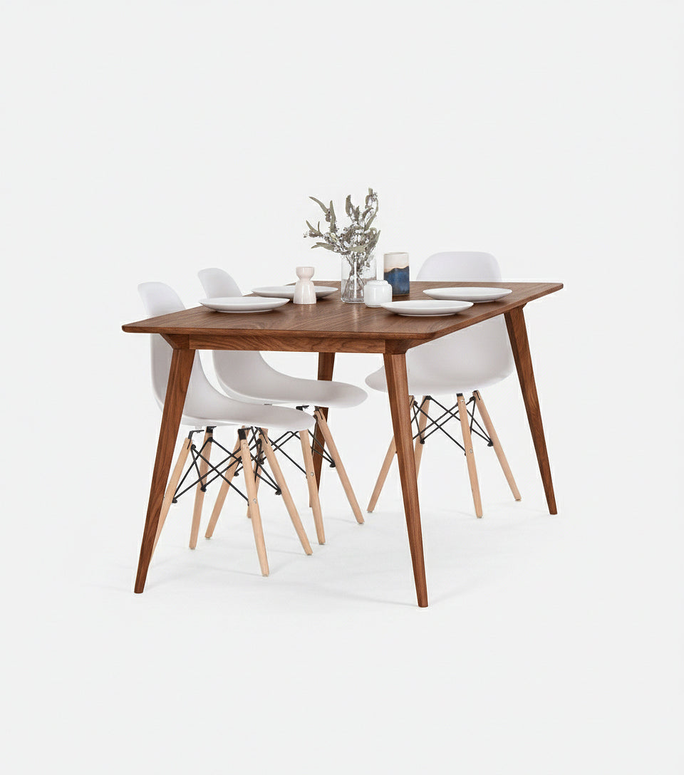 Wooden dining table with four white chairs, set with plates and a small plant centerpiece.