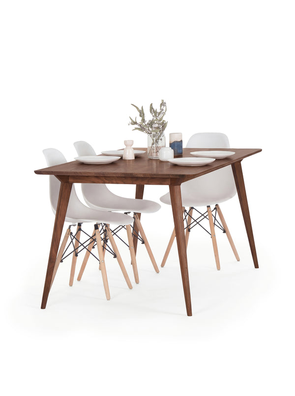 Wooden dining table with four white chairs, set with plates and a small plant centerpiece.