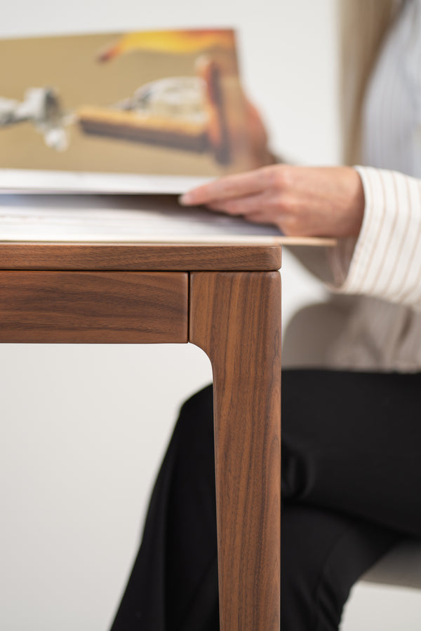 Wooden table close-up with a person holding a book in the background.