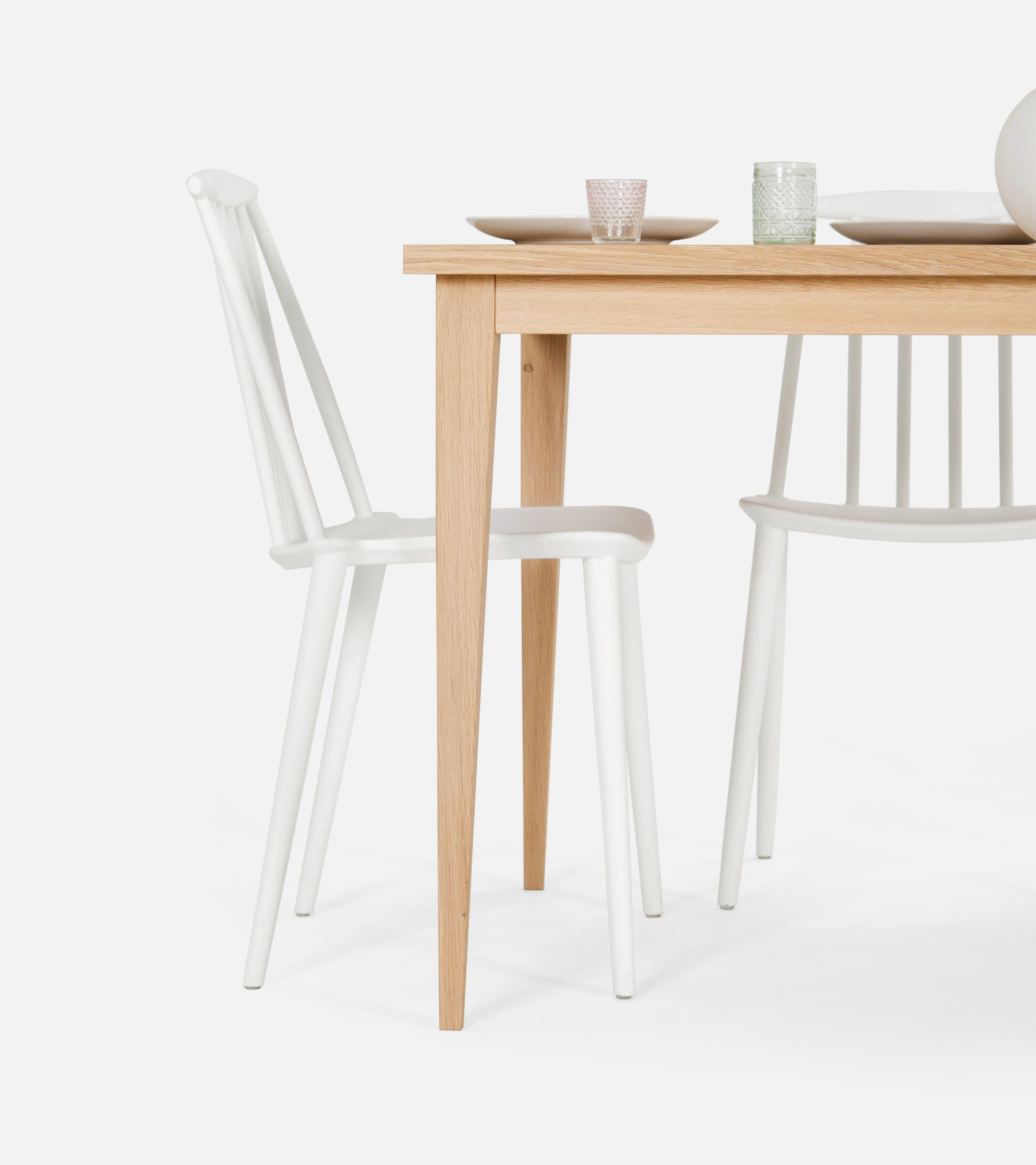 Wooden table with white chairs and simple tableware, including plates and glasses.
