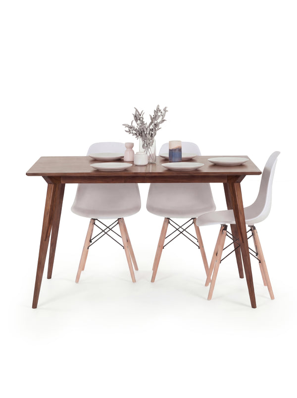 A wooden dining table with white chairs, set with plates, candles, and a vase with branches.