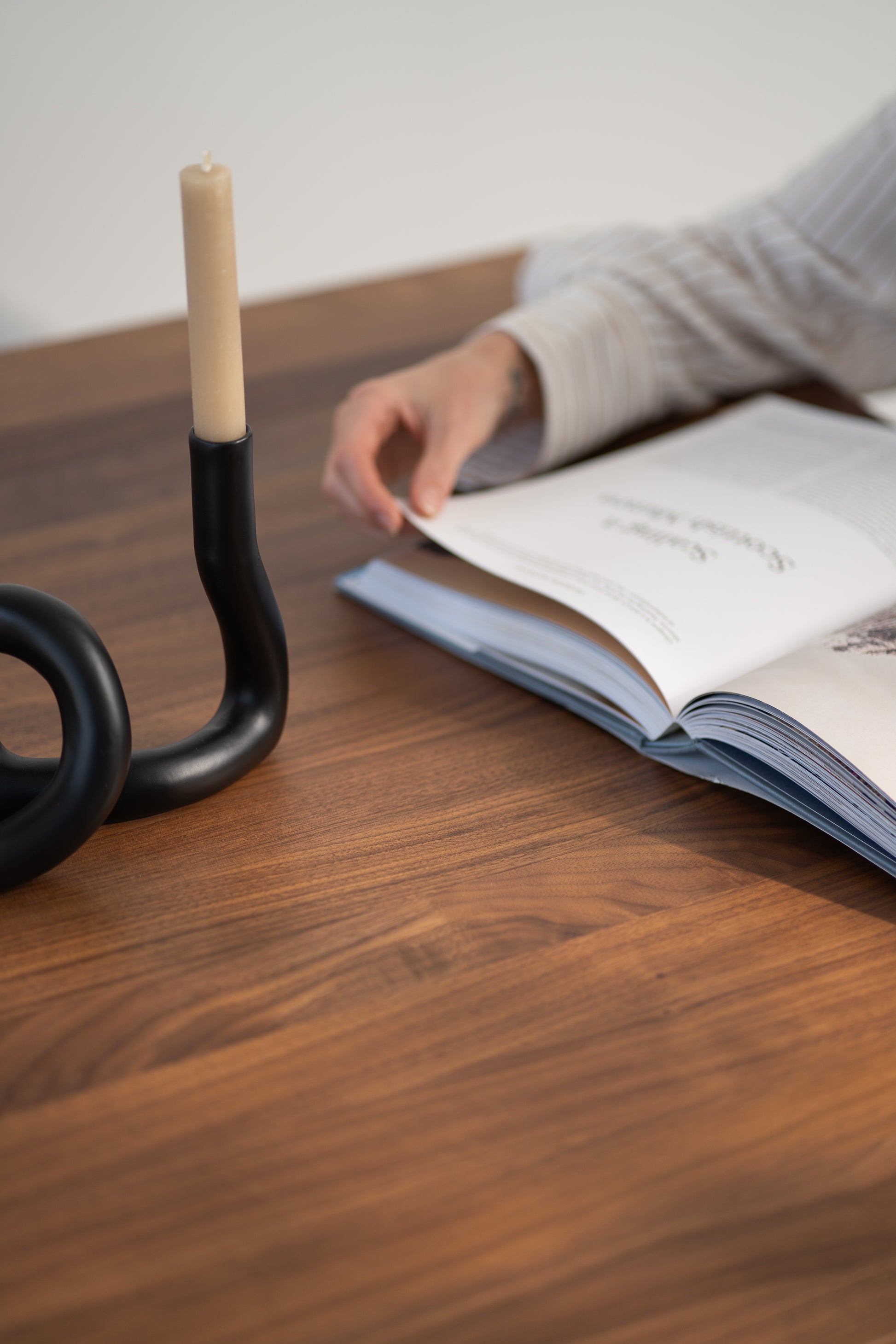 Person reading a magazine at a wooden table with a black candle holder.