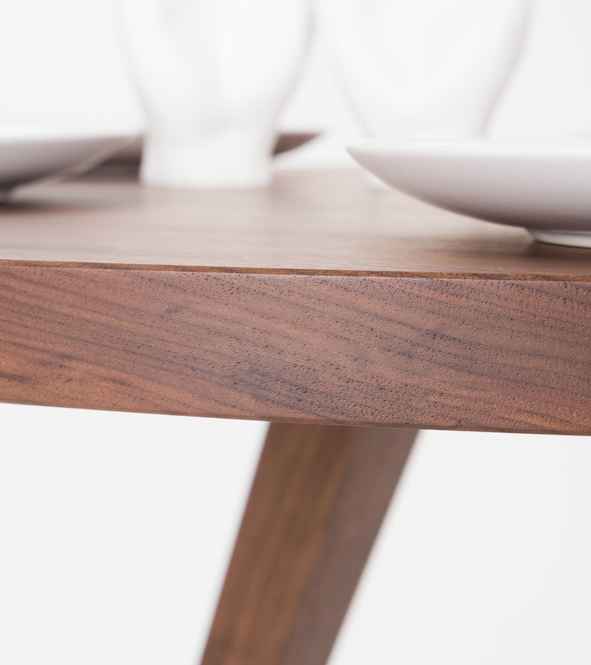 Close-up of a wooden table corner with white ceramic plates and blurry objects in the background.