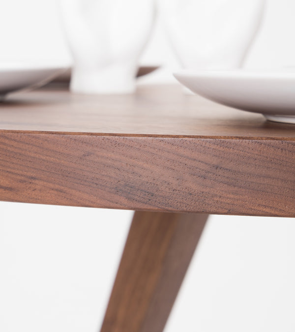 Close-up of a wooden table corner with white ceramic plates and blurry objects in the background.