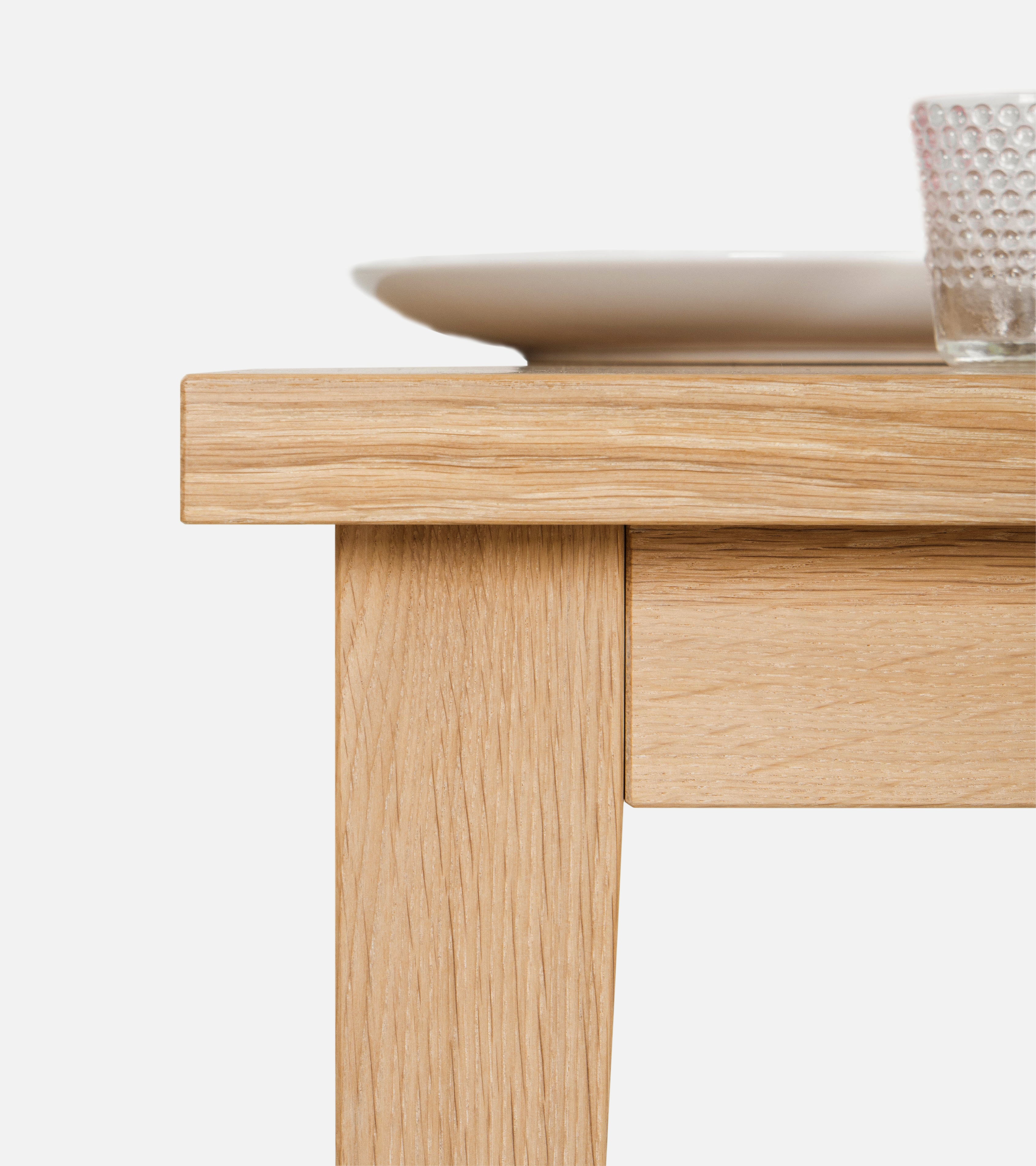 Close-up of a wooden table corner with a white plate and textured glass on top against a white background.