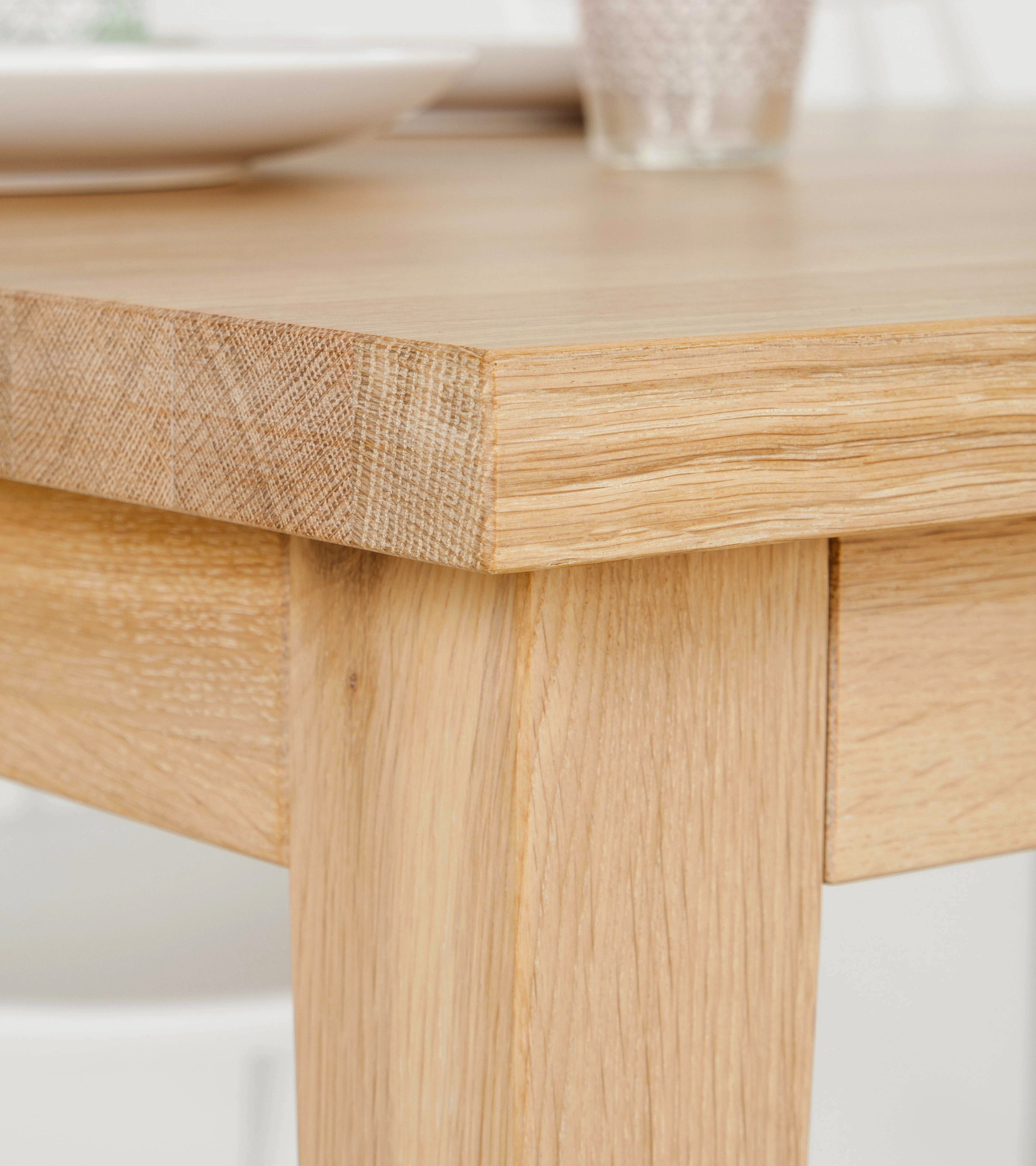 Close-up of the corner of a wooden table with plates and a glass in the background.