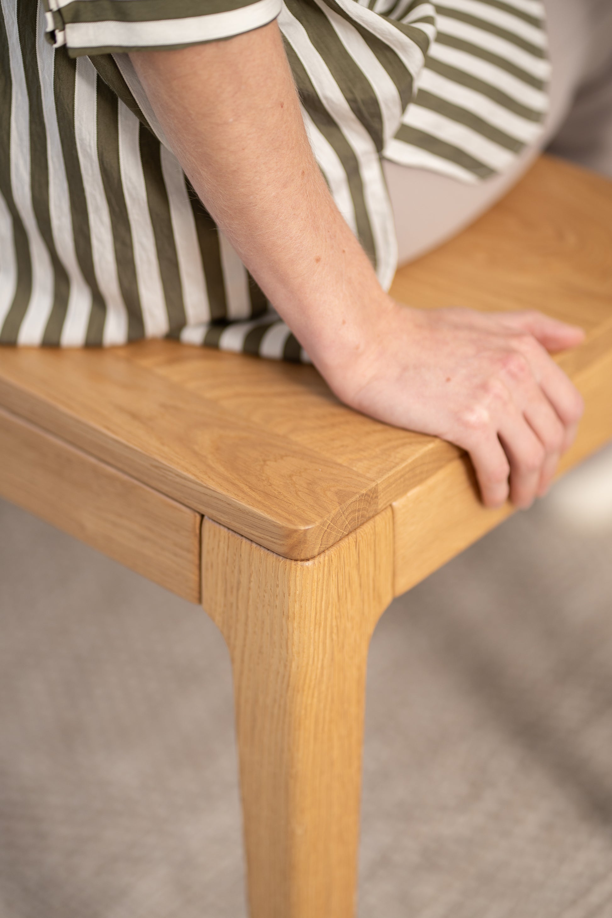 Person sitting on a wooden bench, wearing a green and white striped garment.