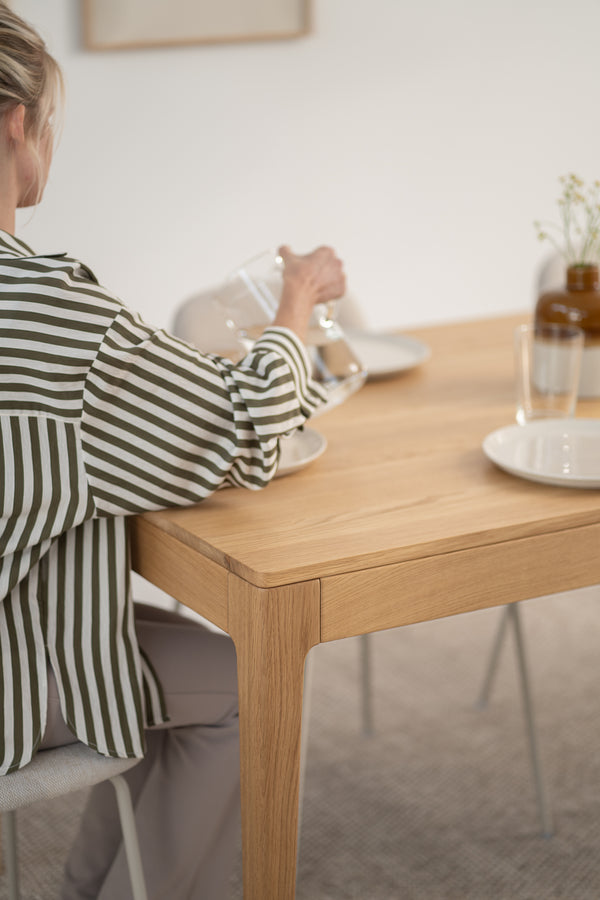 Person in striped shirt pours water at a wooden table set with plates and a vase.