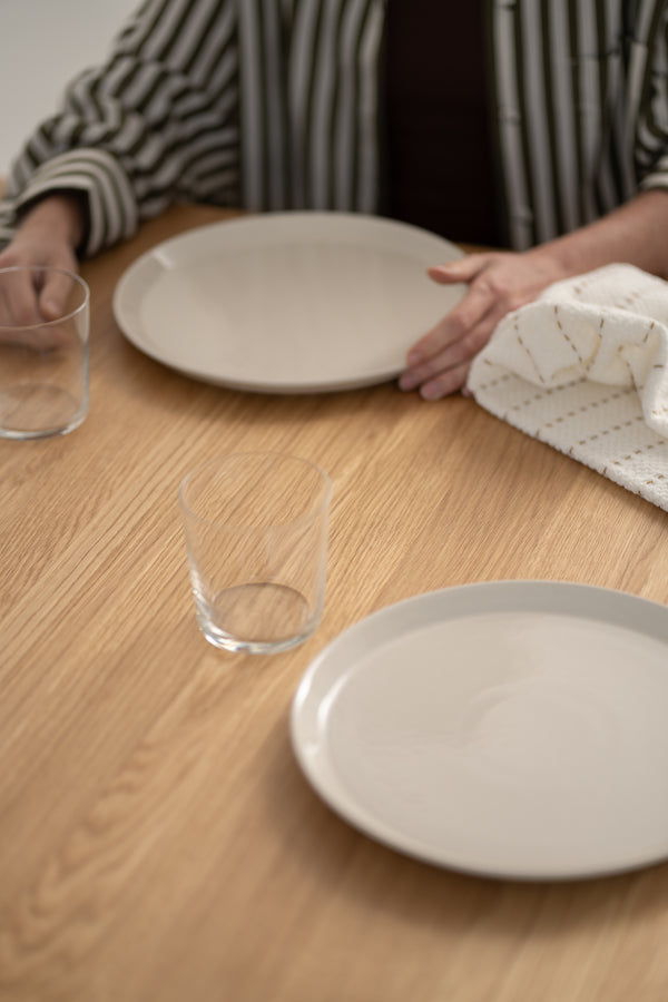 Hands setting plates and glasses on a wooden table.