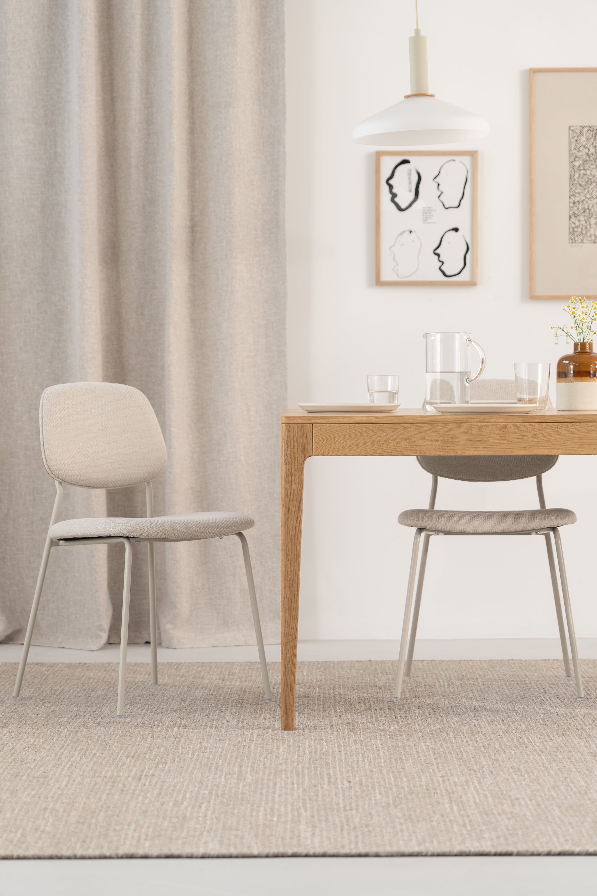 Minimalist dining area with a wooden table, two chairs, pendant light, and abstract wall art.