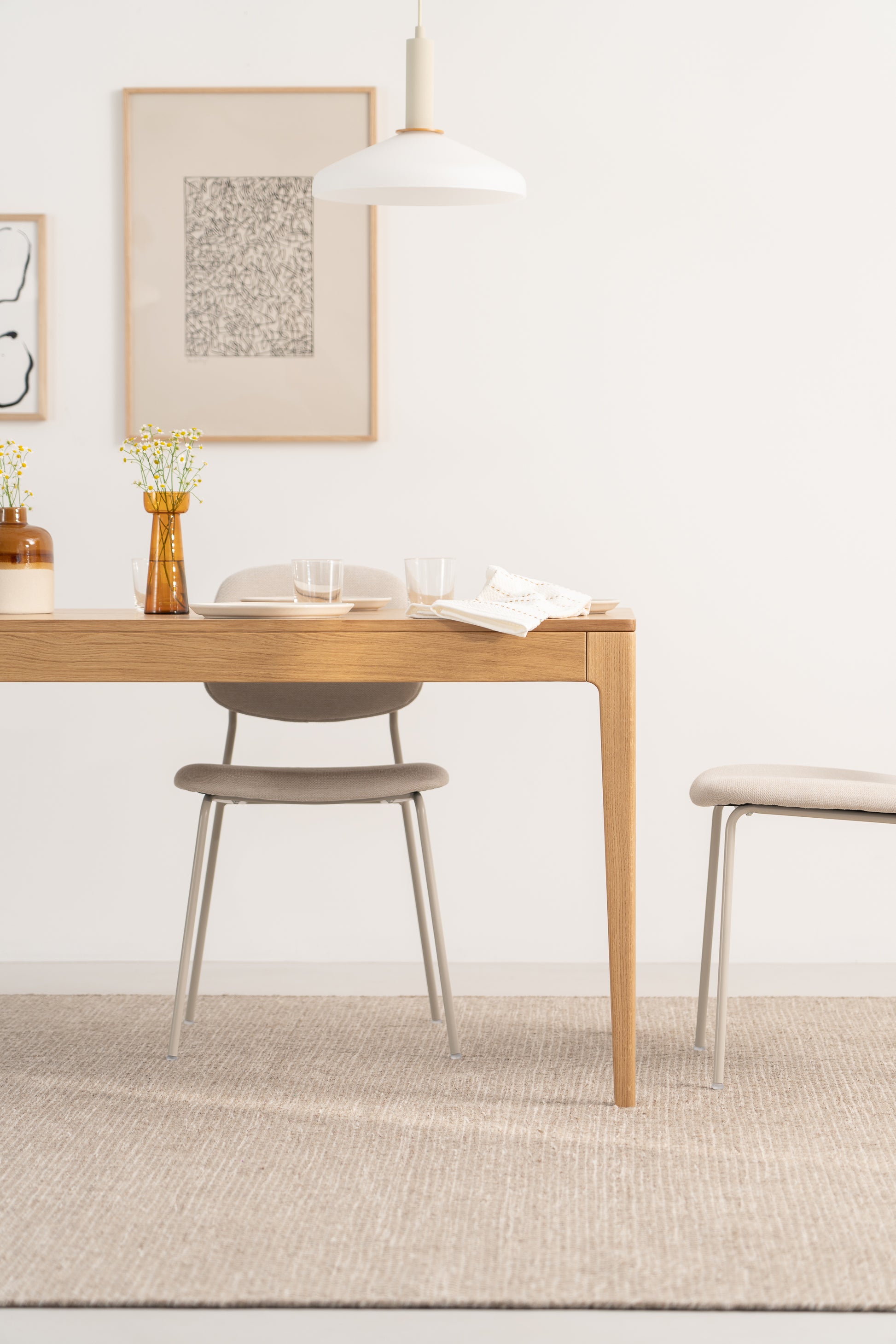 Minimalist dining area with wooden table, beige chairs, and wall art.
