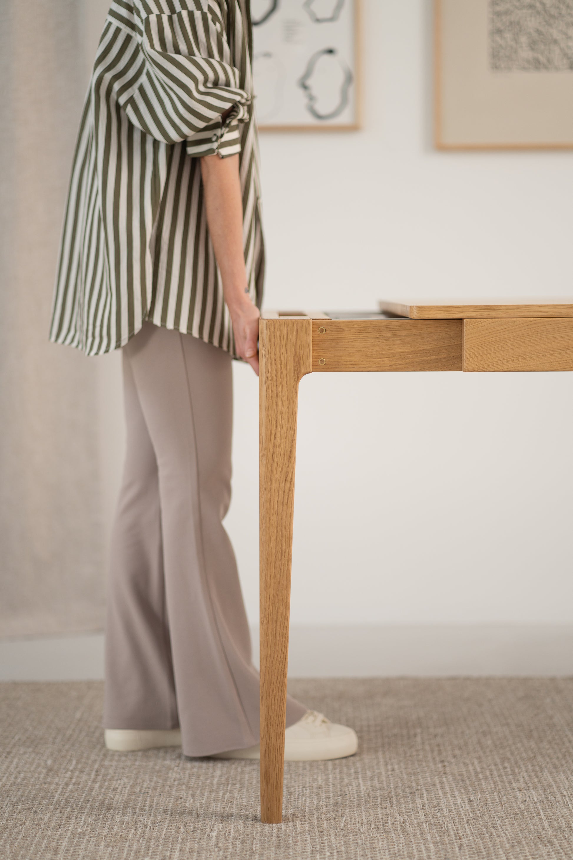 Person in striped shirt and flared pants adjusting a wooden table in a room.