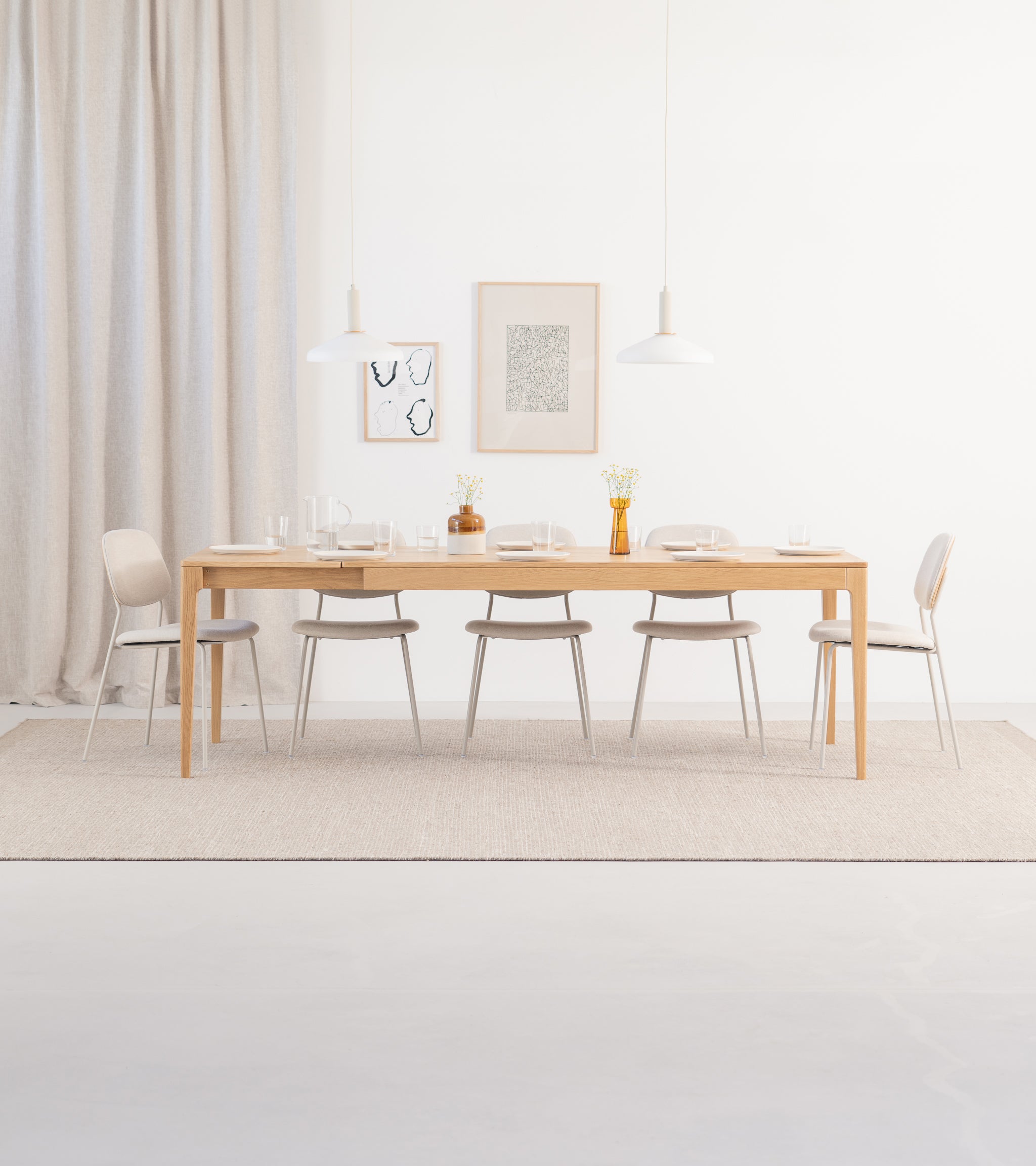 Minimalist dining room with a wooden table, six chairs, pendant lights, and wall art.