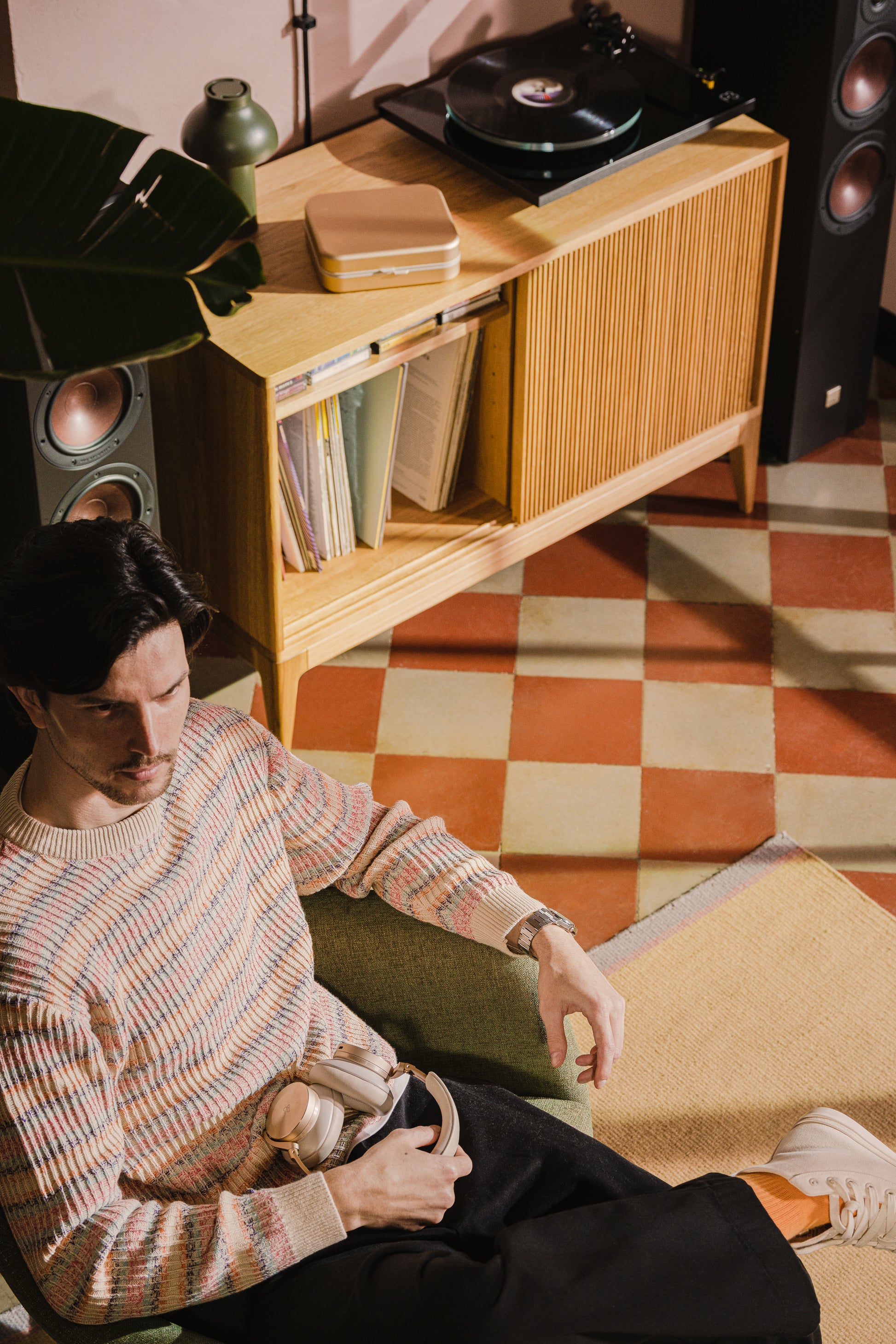 Seated man with headphones in retro room, vinyl playing on a wooden console.