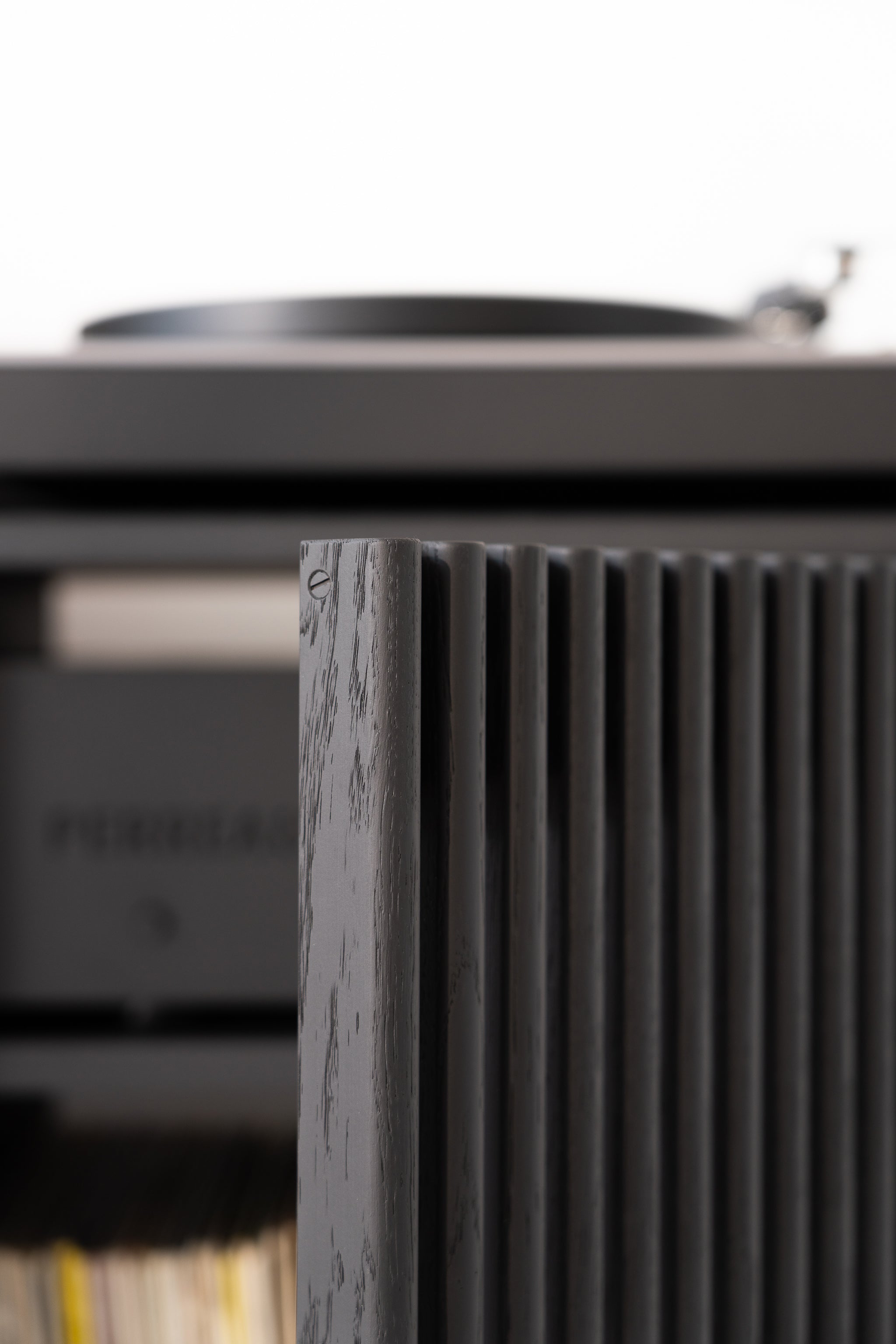 Close-up of a textured wooden panel with a blurred black turntable in the background.