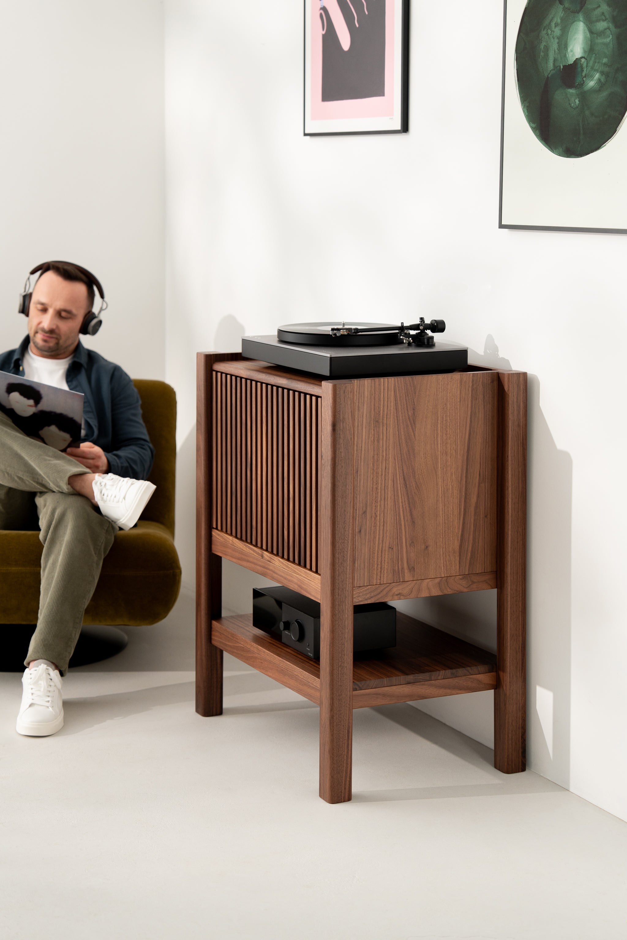 Man relaxing with headphones, a vinyl record, and a wooden turntable stand in a modern room.