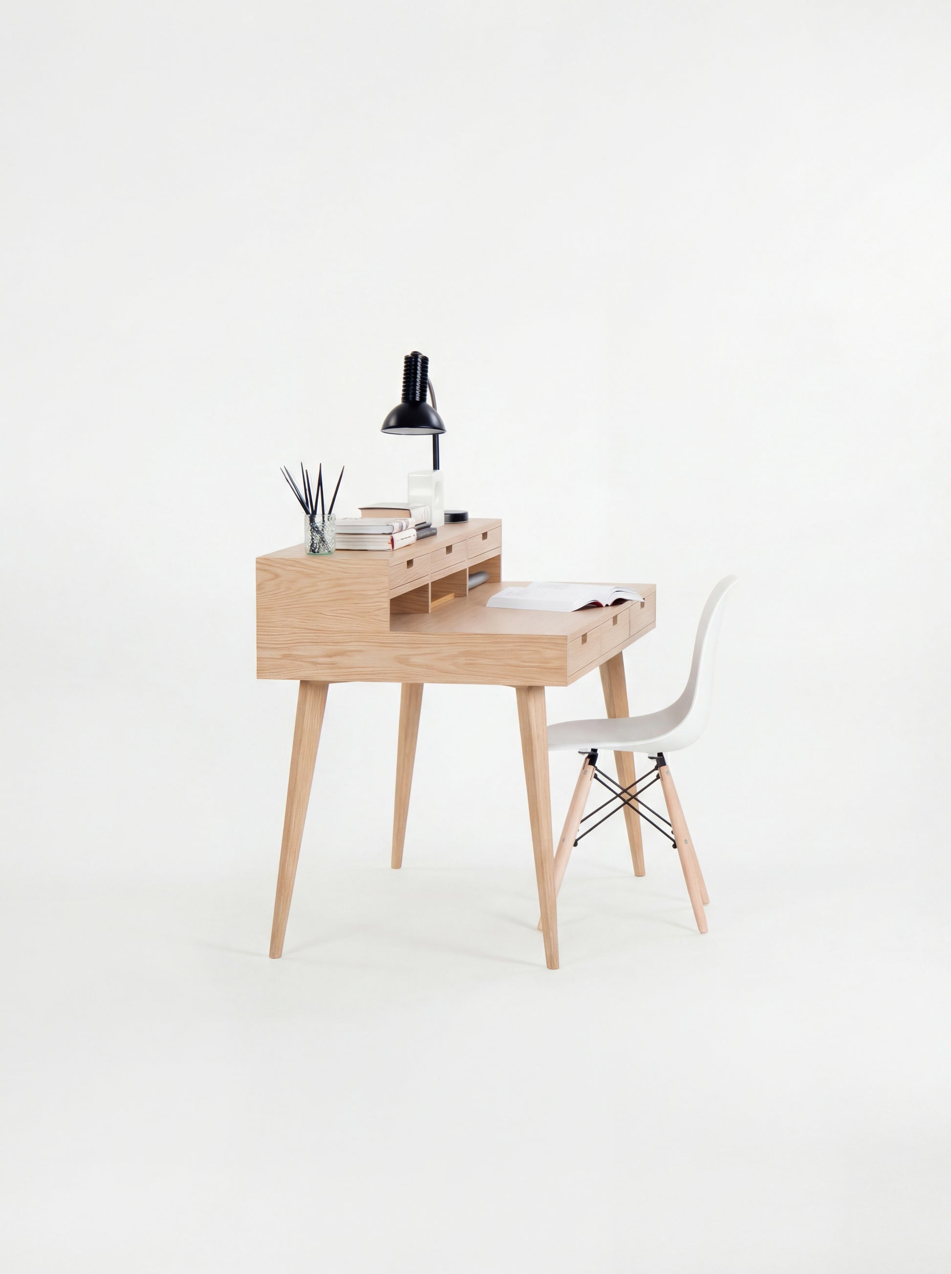 Wooden desk with a black lamp, books, and small decor, paired with a white chair.