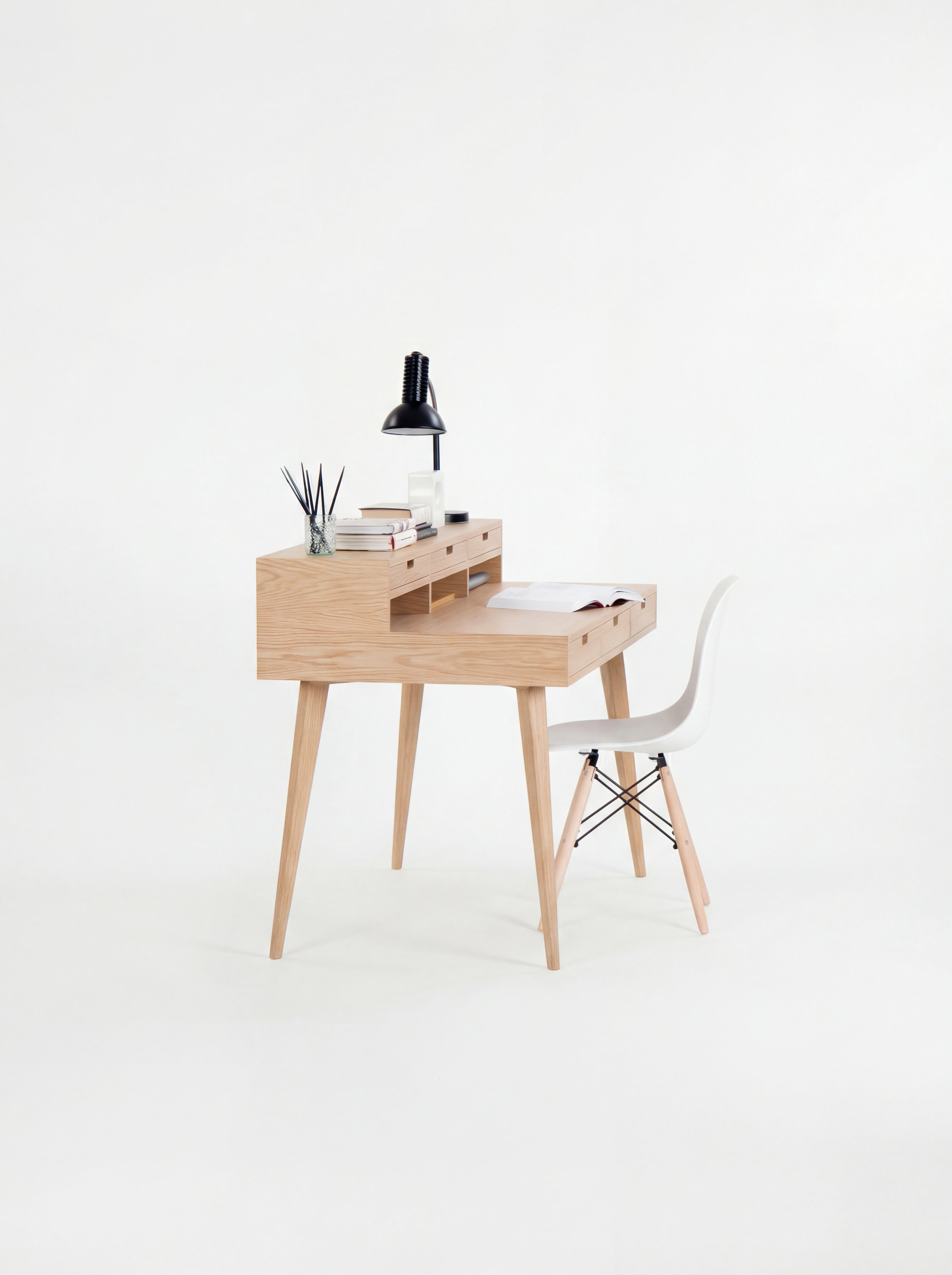 Wooden desk with a black lamp, books, and small decor, paired with a white chair.