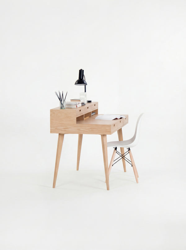 Wooden desk with a black lamp, books, and small decor, paired with a white chair.