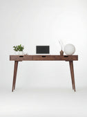 HEIM 140 wooden desk with drawers in walnut wood, shown from the front with a laptop and globe lamp