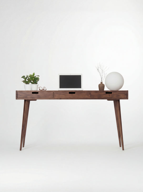 HEIM 140 wooden desk with drawers in walnut wood, shown from the front with a laptop and globe lamp