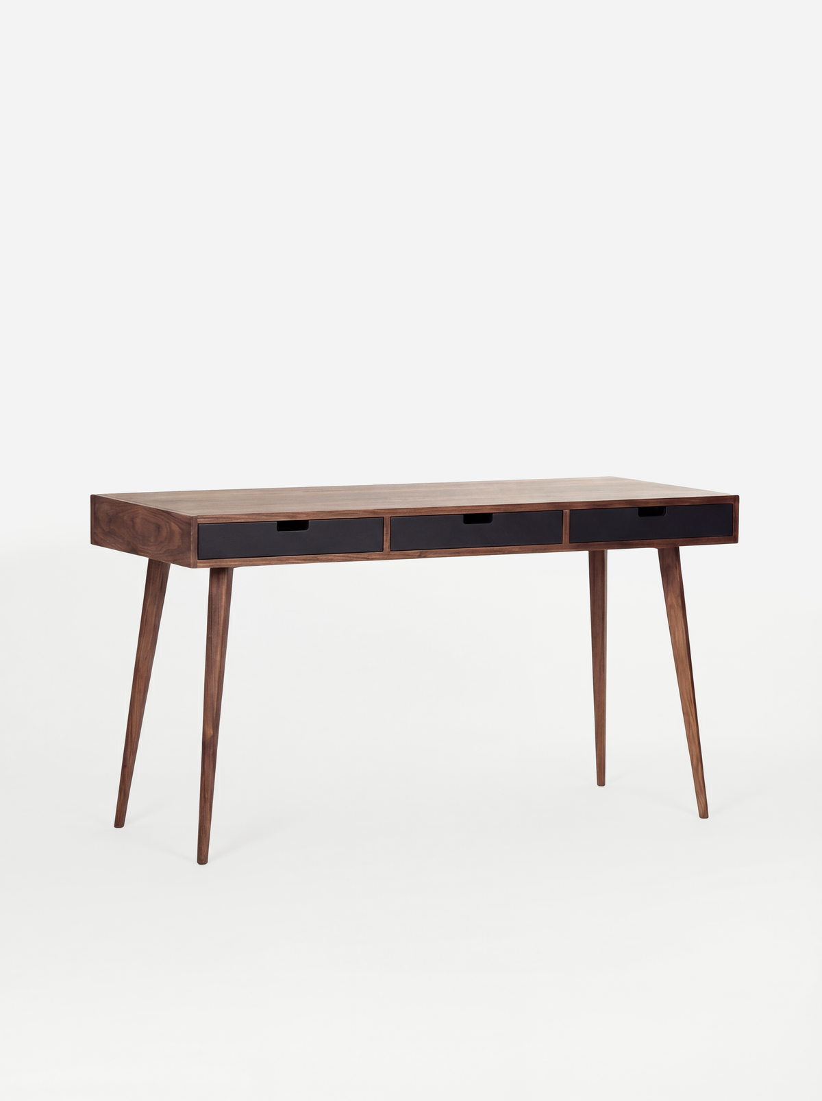 Angled view of the empty HEIM 140 desk in walnut wood, with three black drawer fronts against a white background