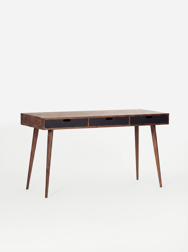 Angled view of the empty HEIM 140 desk in walnut wood, with three black drawer fronts against a white background