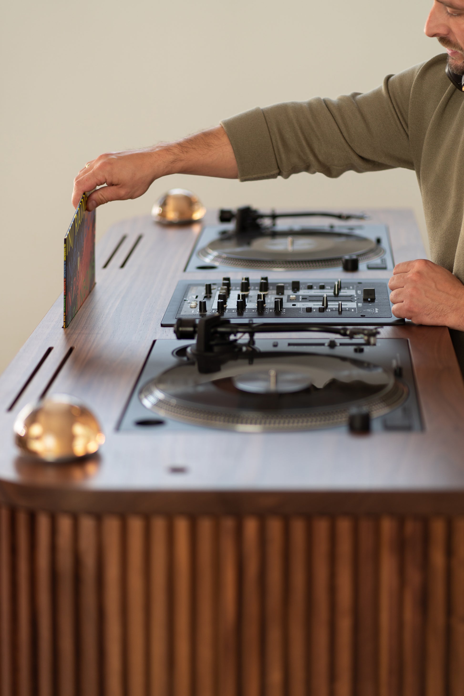 Person placing a vinyl record into a wooden DJ setup with turntables and a mixer.