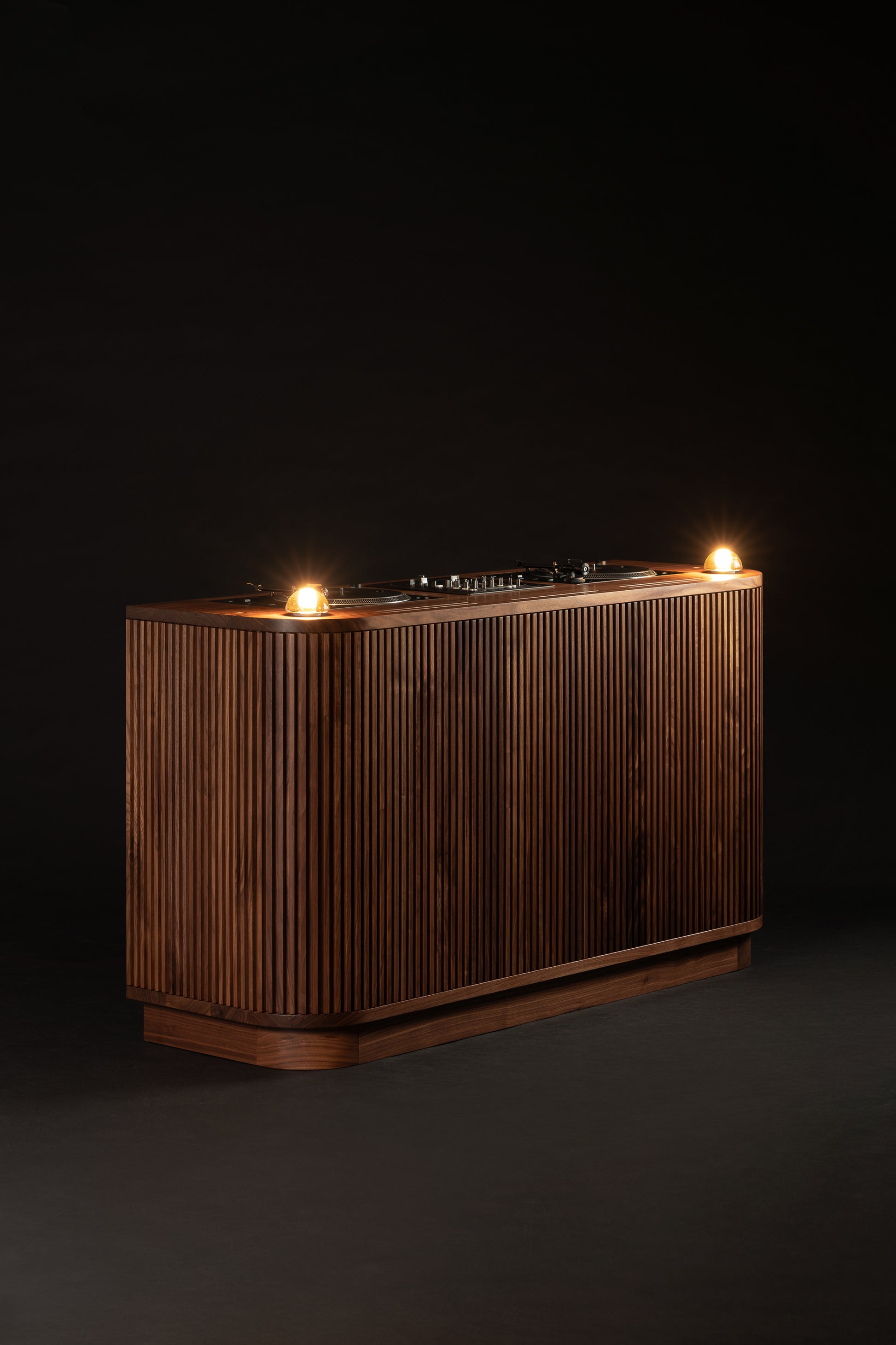 Wooden DJ console with a ribbed design and two glowing lights on top, set against a dark background.