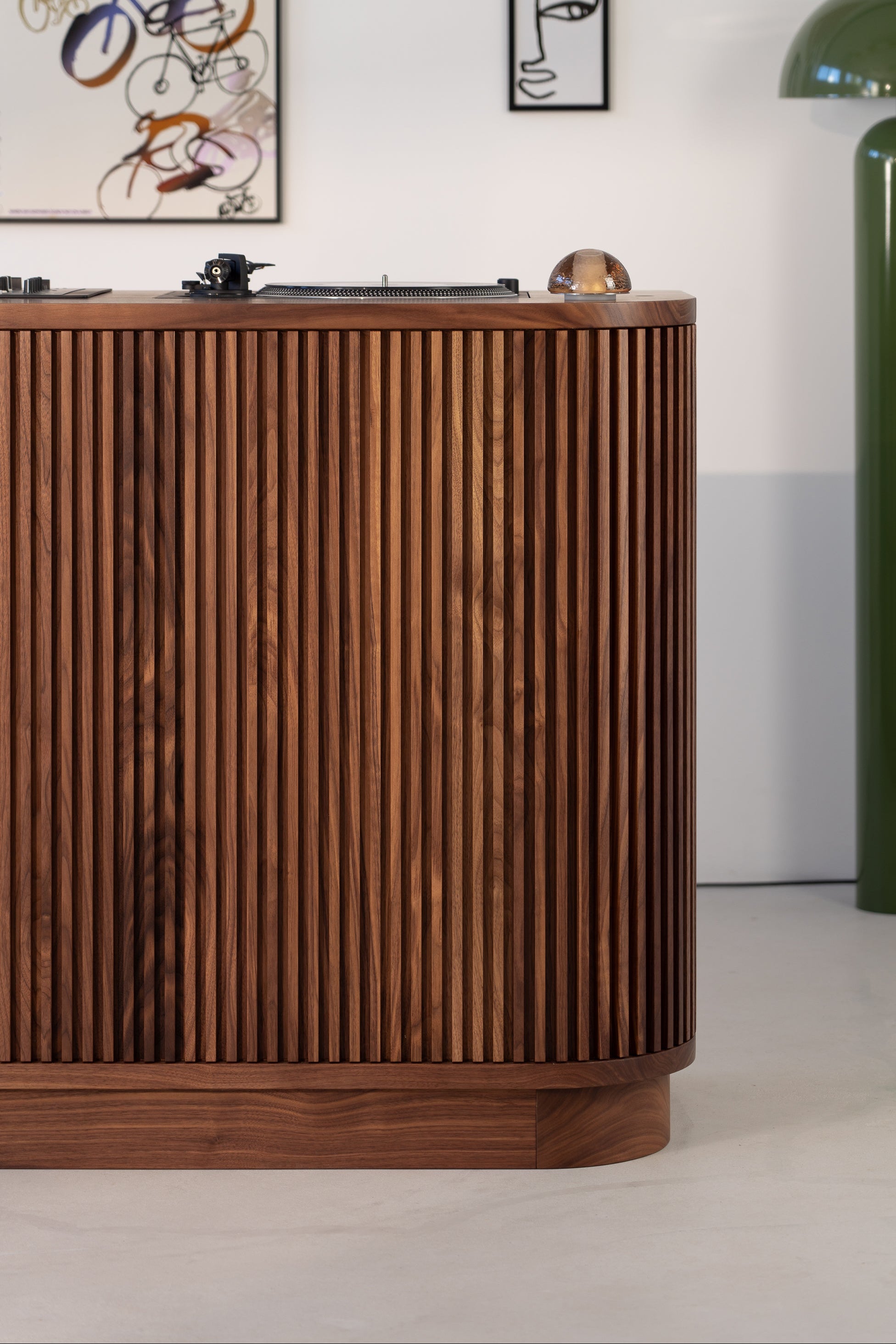 Wooden sideboard with vertical slats, green lamp, and two abstract wall art pieces.