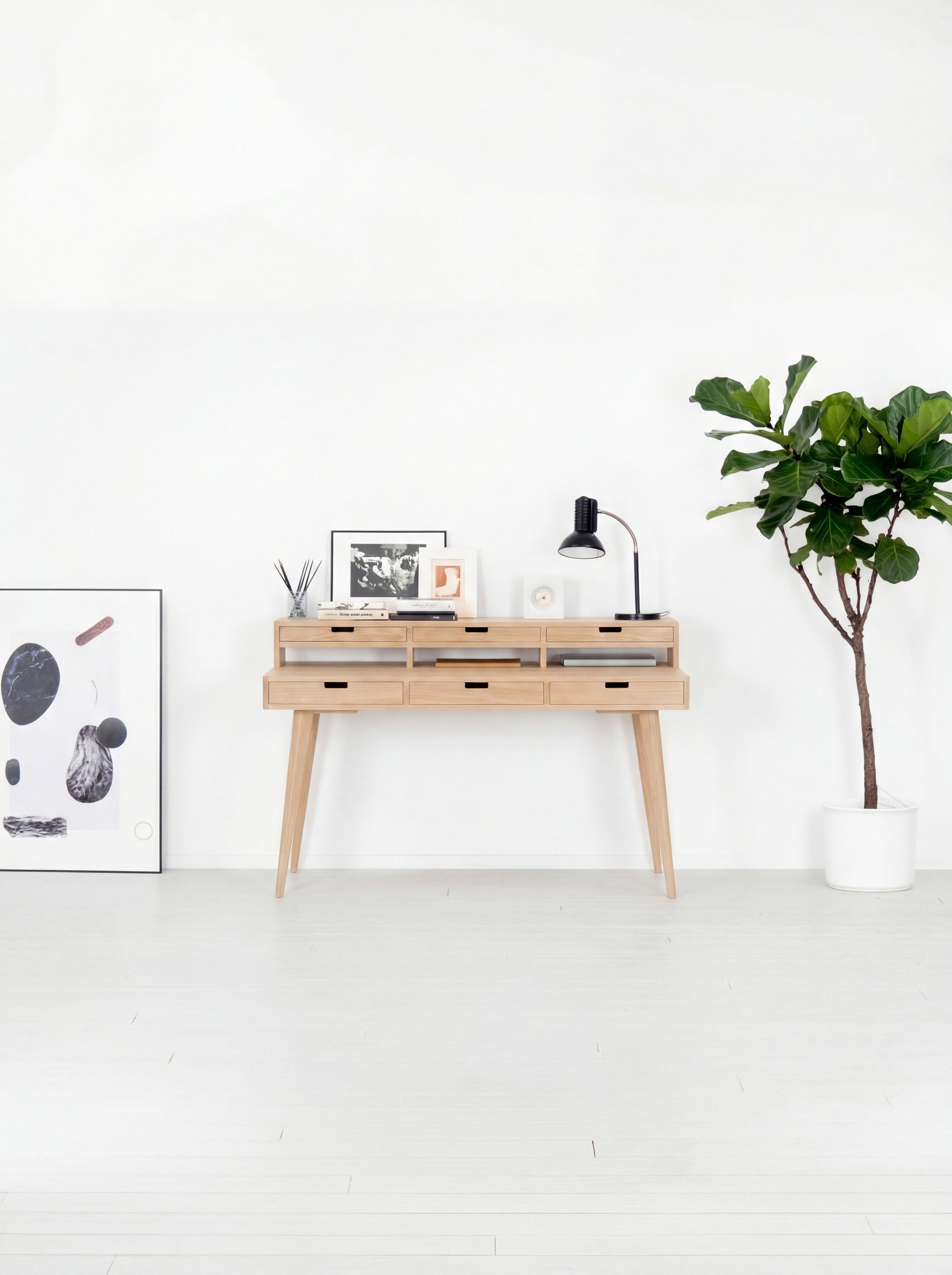 Minimalist room with a wooden console table, lamp, art, and plant on a white wall.